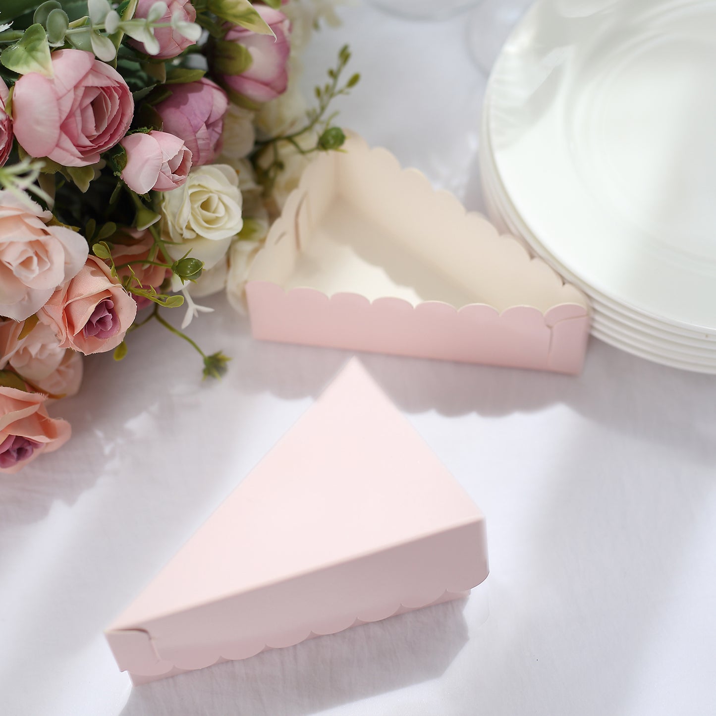 Blush triangular paper cake boxes with scalloped top on a white table.