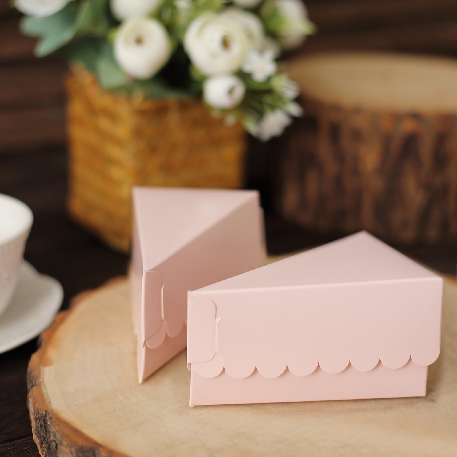 Blush triangular paper cake boxes with scalloped tops on a wooden surface.