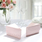 Blush triangular paper cake boxes on a table with flowers and glassware.