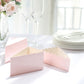 Blush triangular paper cake boxes with scalloped top on a table setting.