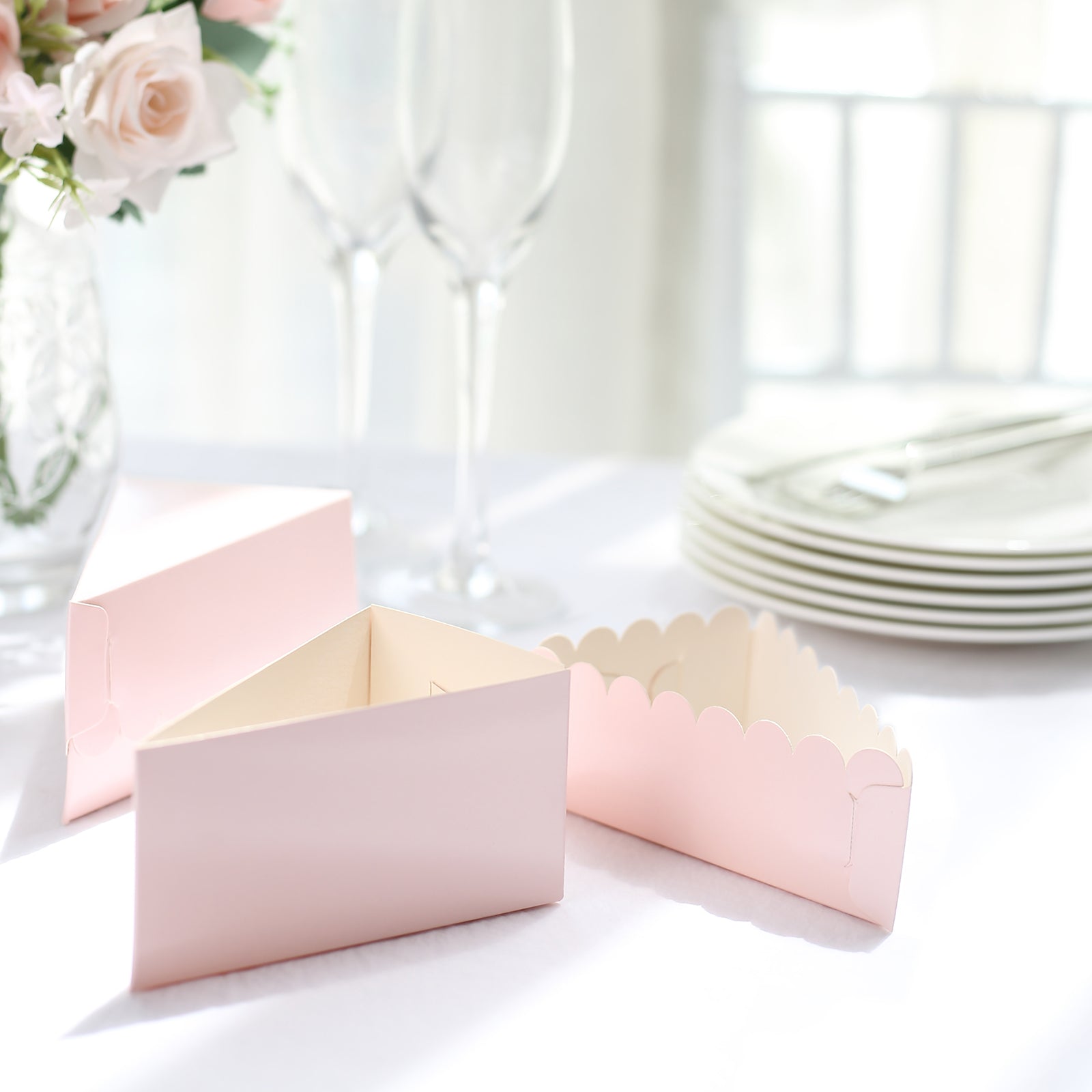 Blush triangular paper cake boxes with scalloped top on a table setting.