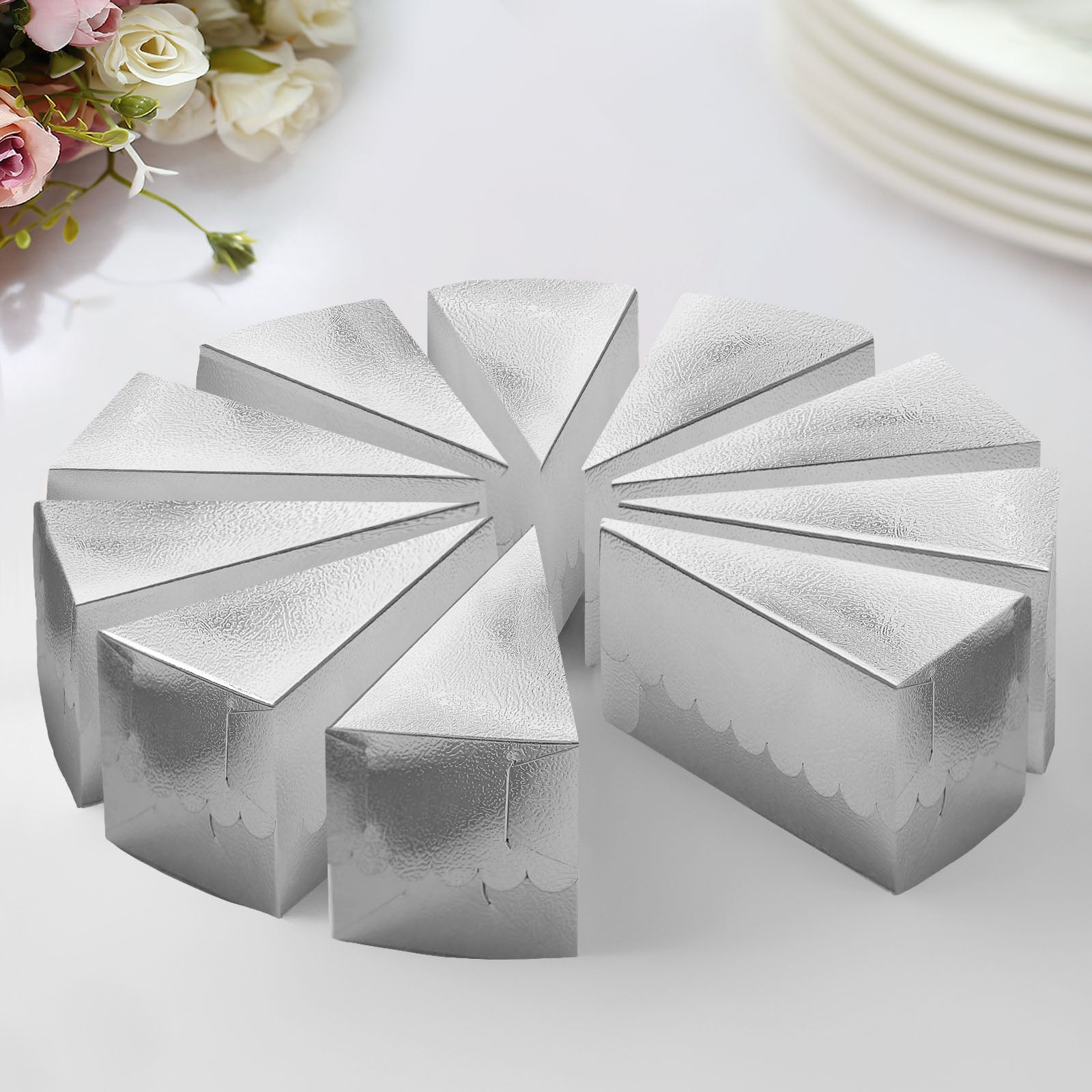 Metallic silver triangular cake boxes arranged in a circle on a table.