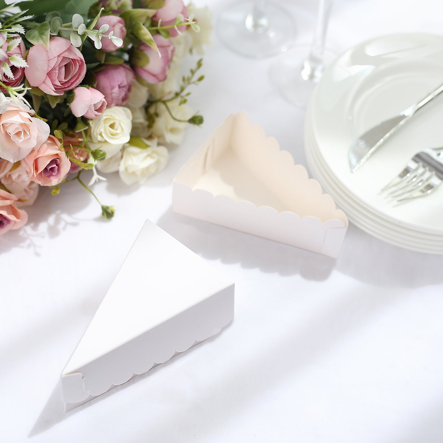 White triangular paper cake boxes with scalloped tops on a table.