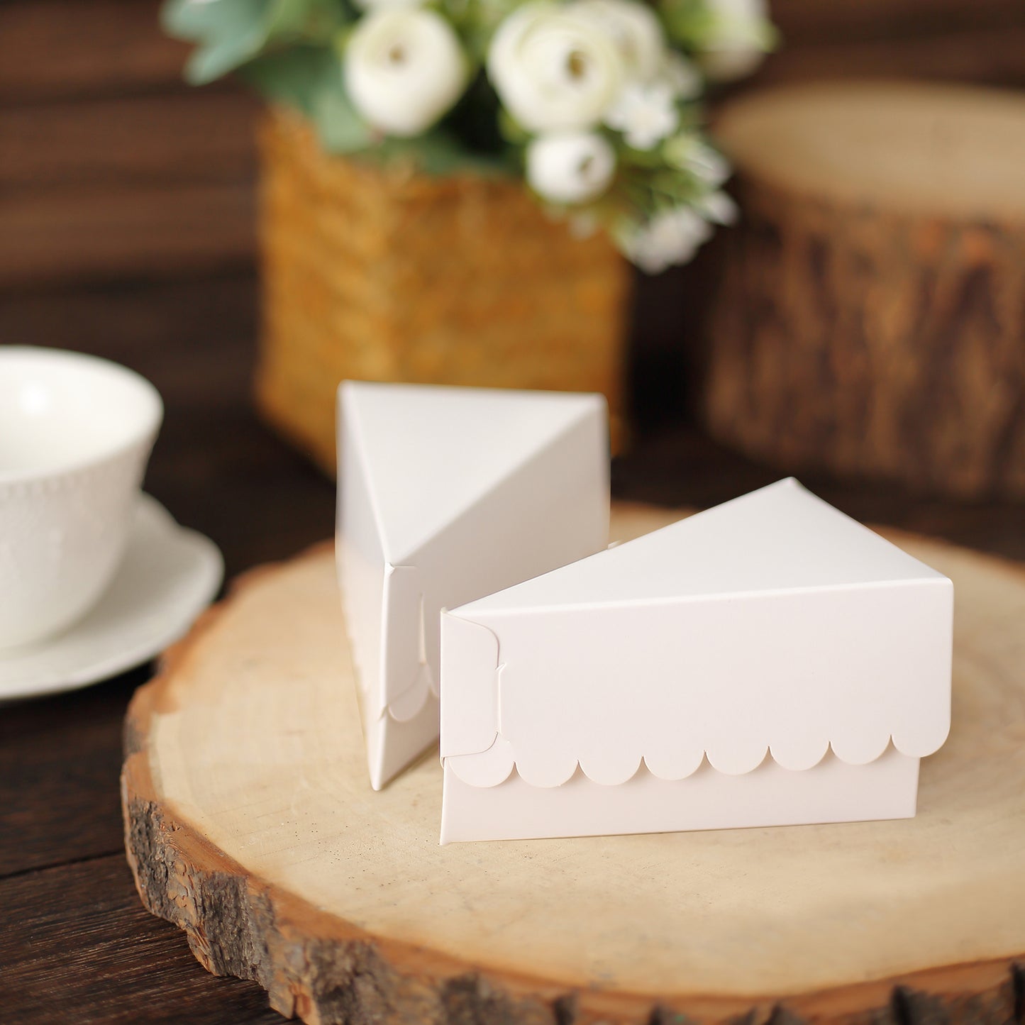 White triangular paper cake boxes with scalloped tops on a wooden surface.