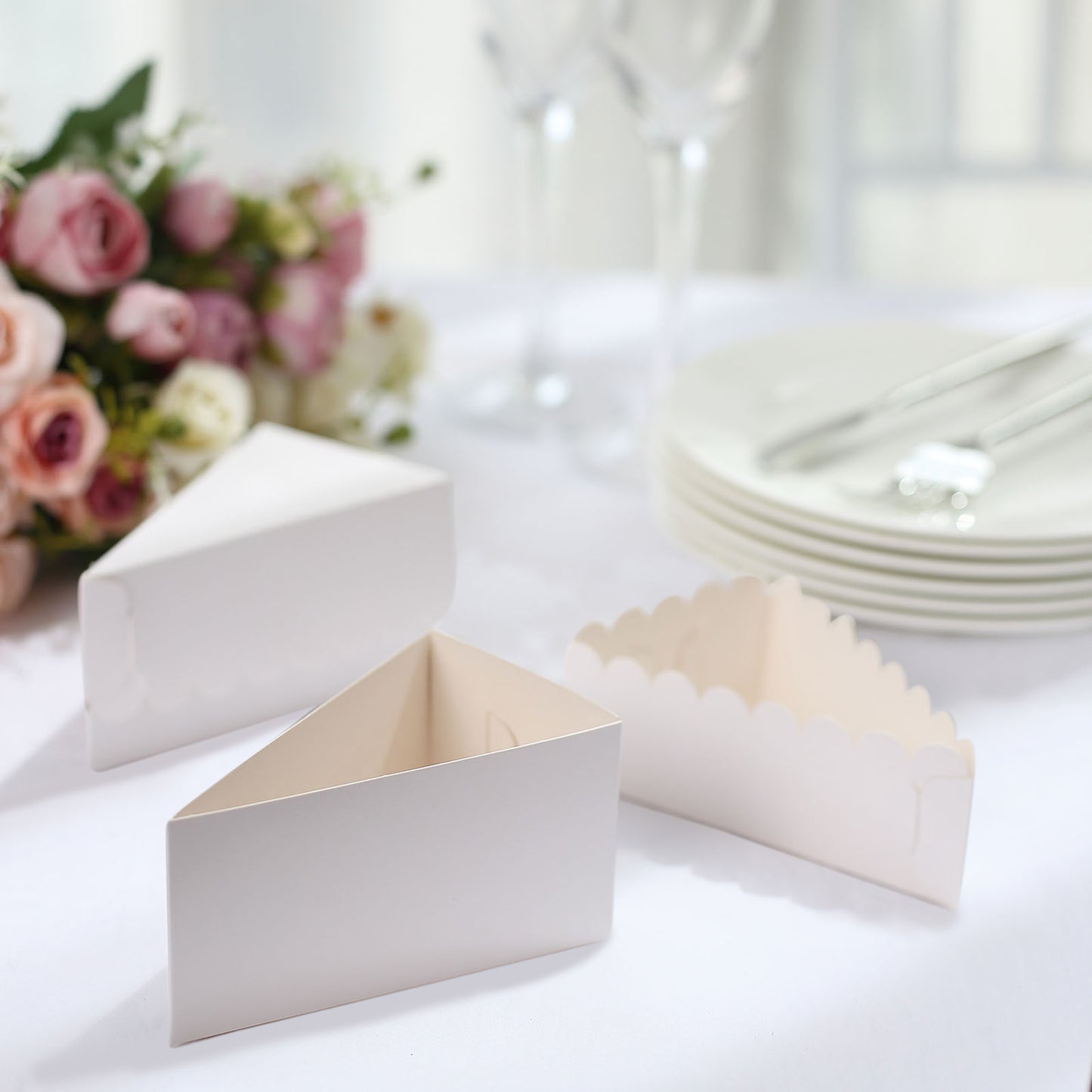 White triangular paper cake boxes with scalloped tops on a table.