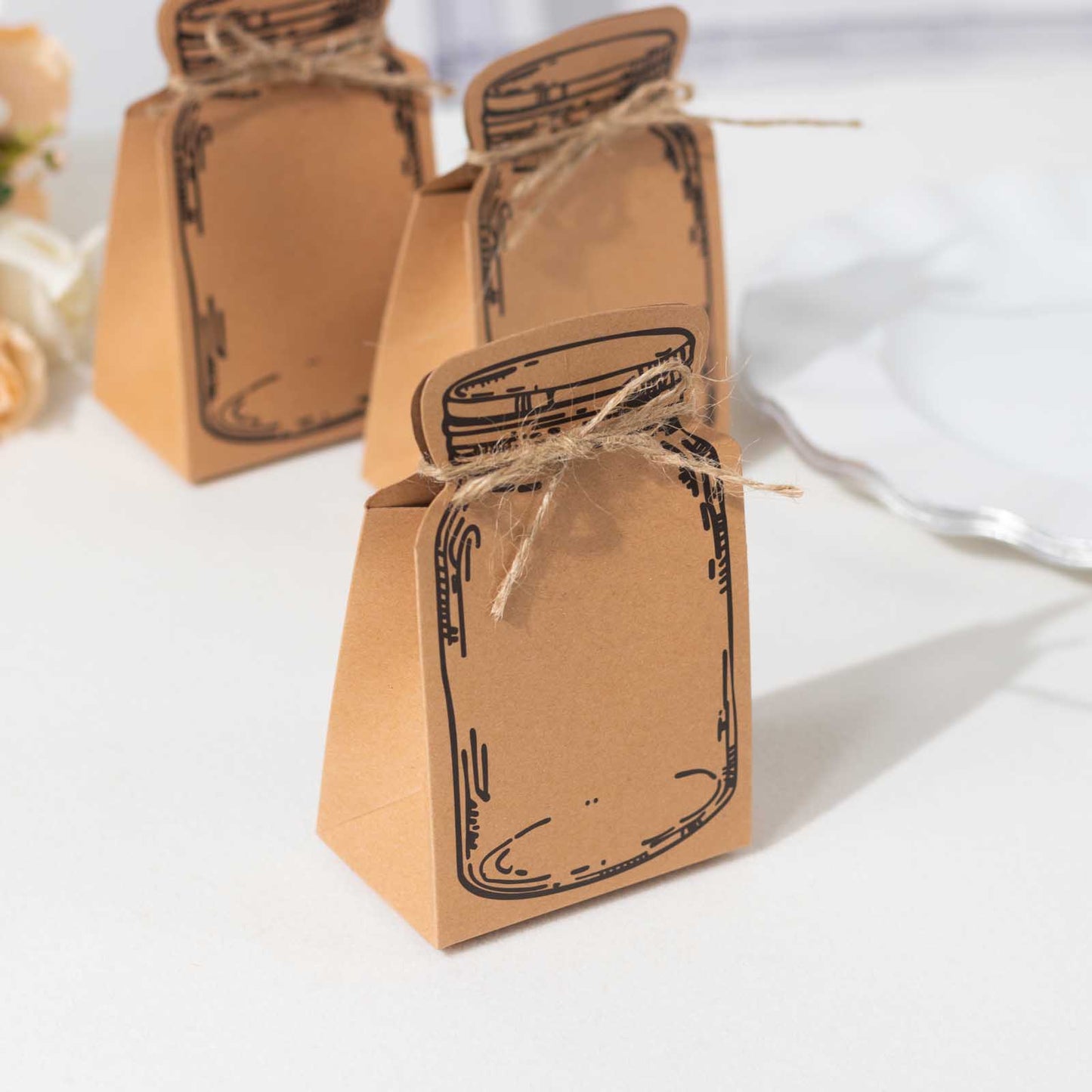 Natural mini mason jar shaped paper party favor boxes in brown with jute rope ties.