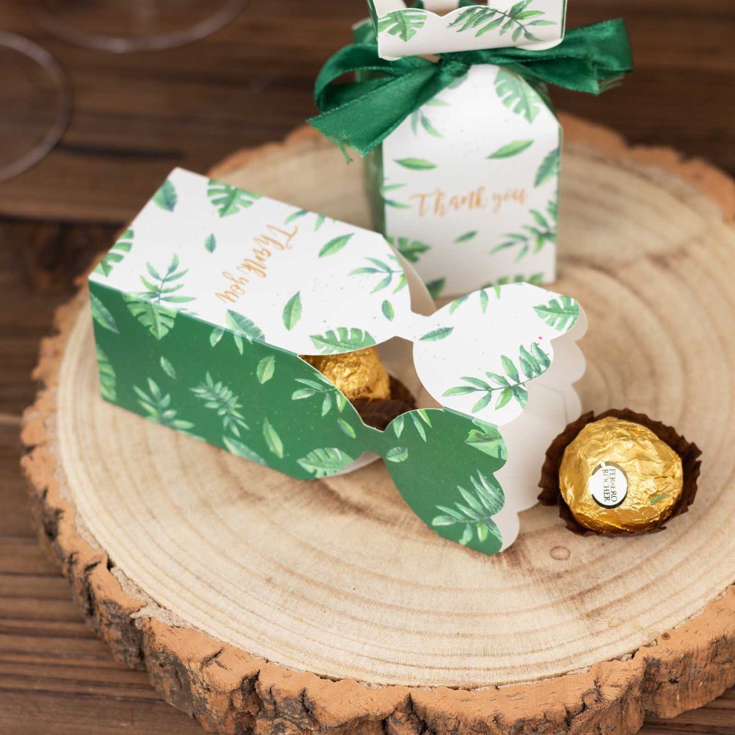 White and green leaf print satin ribbon gift boxes on a wooden surface.