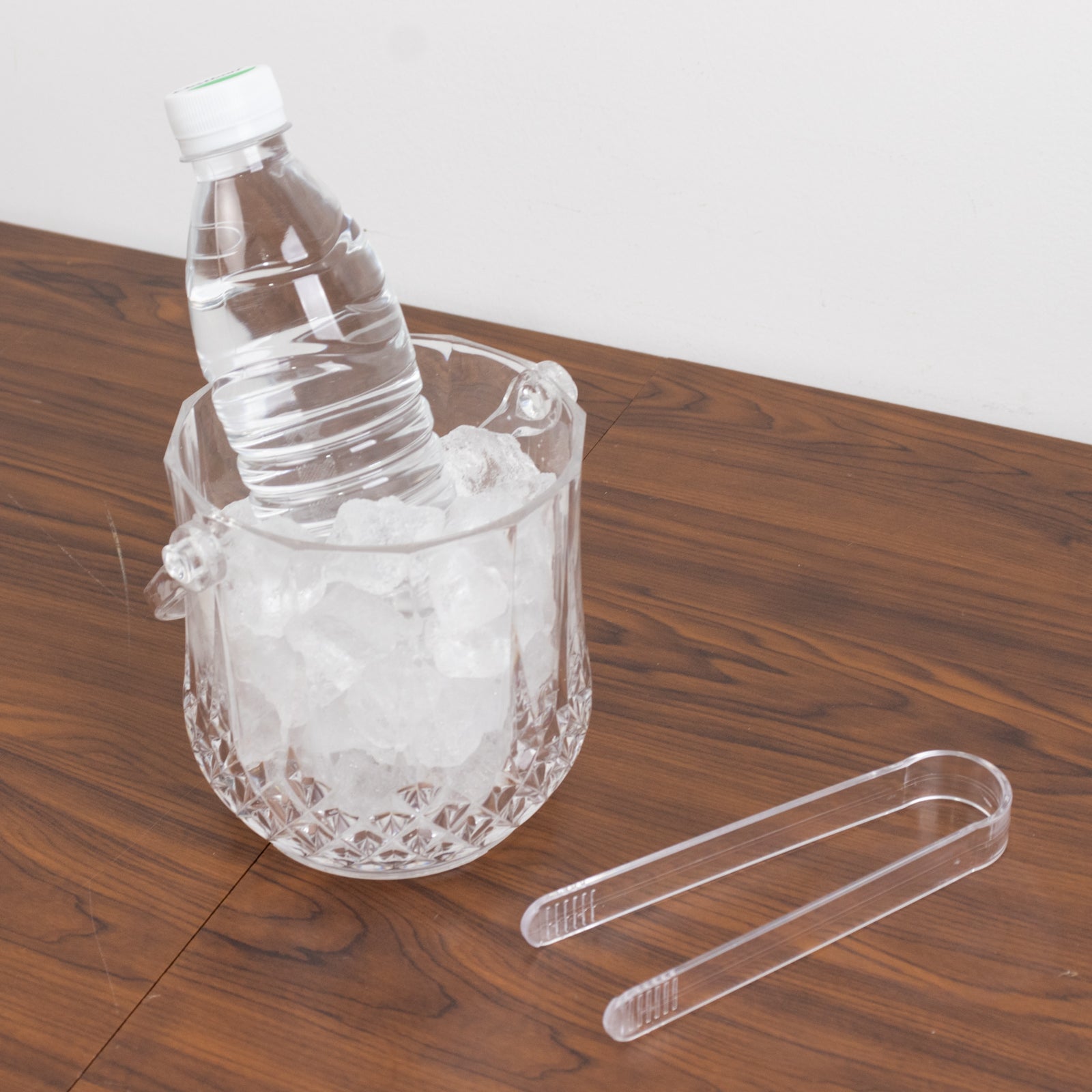 Clear plastic ice bucket with handle and tongs, filled with ice and a water bottle.
