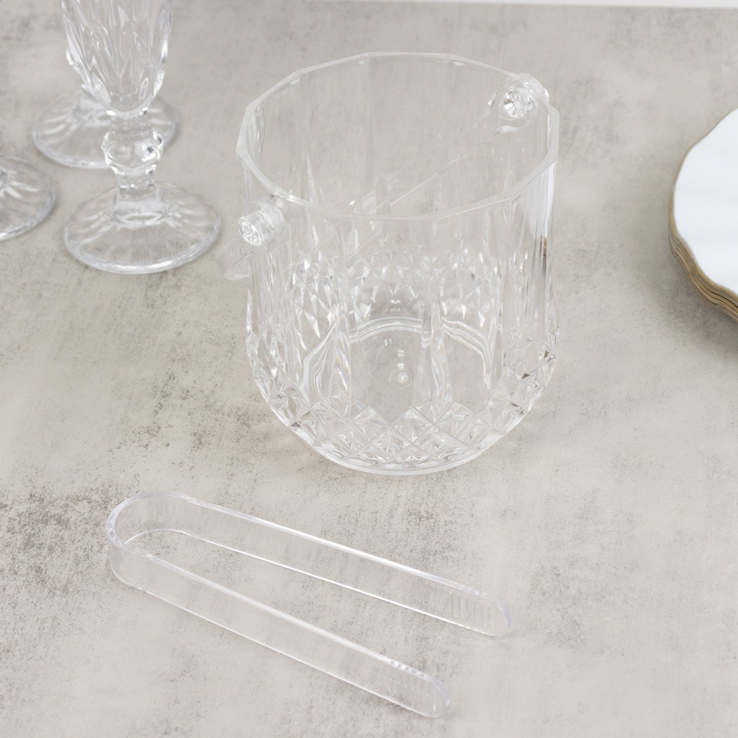 Clear plastic ice bucket with tongs in crystal-cut design for drinks.