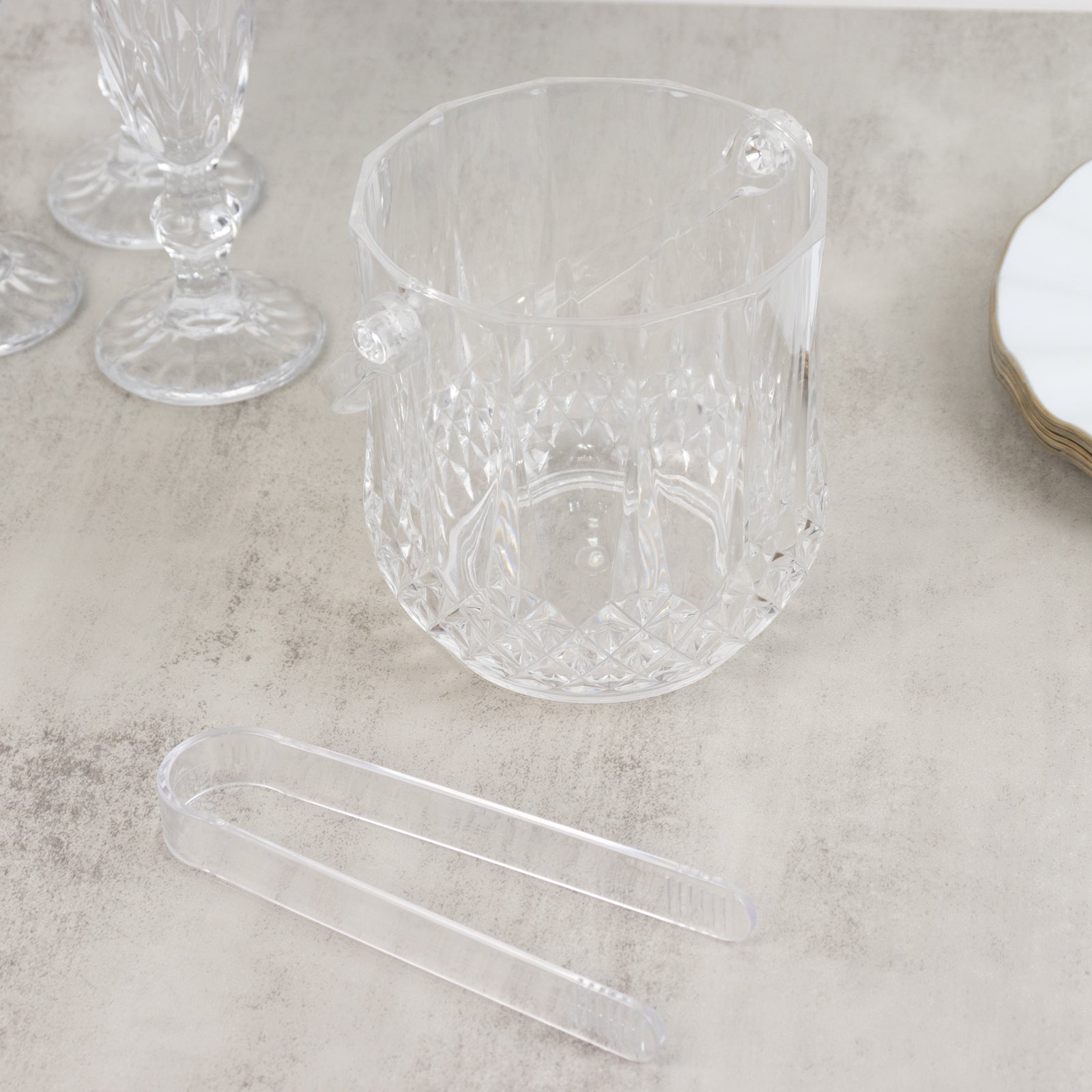 Clear plastic ice bucket with tongs in crystal-cut design for drinks.
