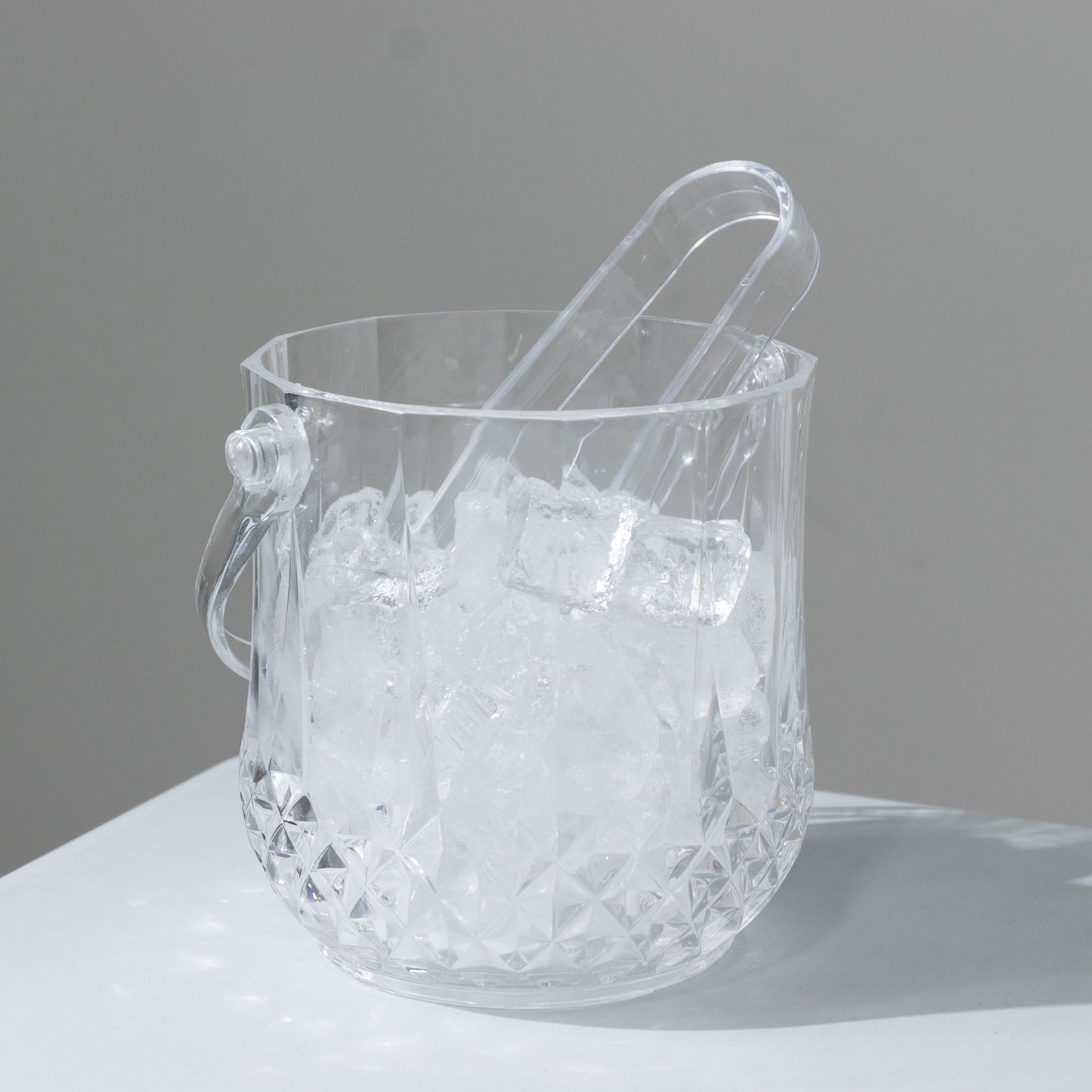 Clear plastic ice bucket with tongs in crystal-cut design, perfect for cocktails.
