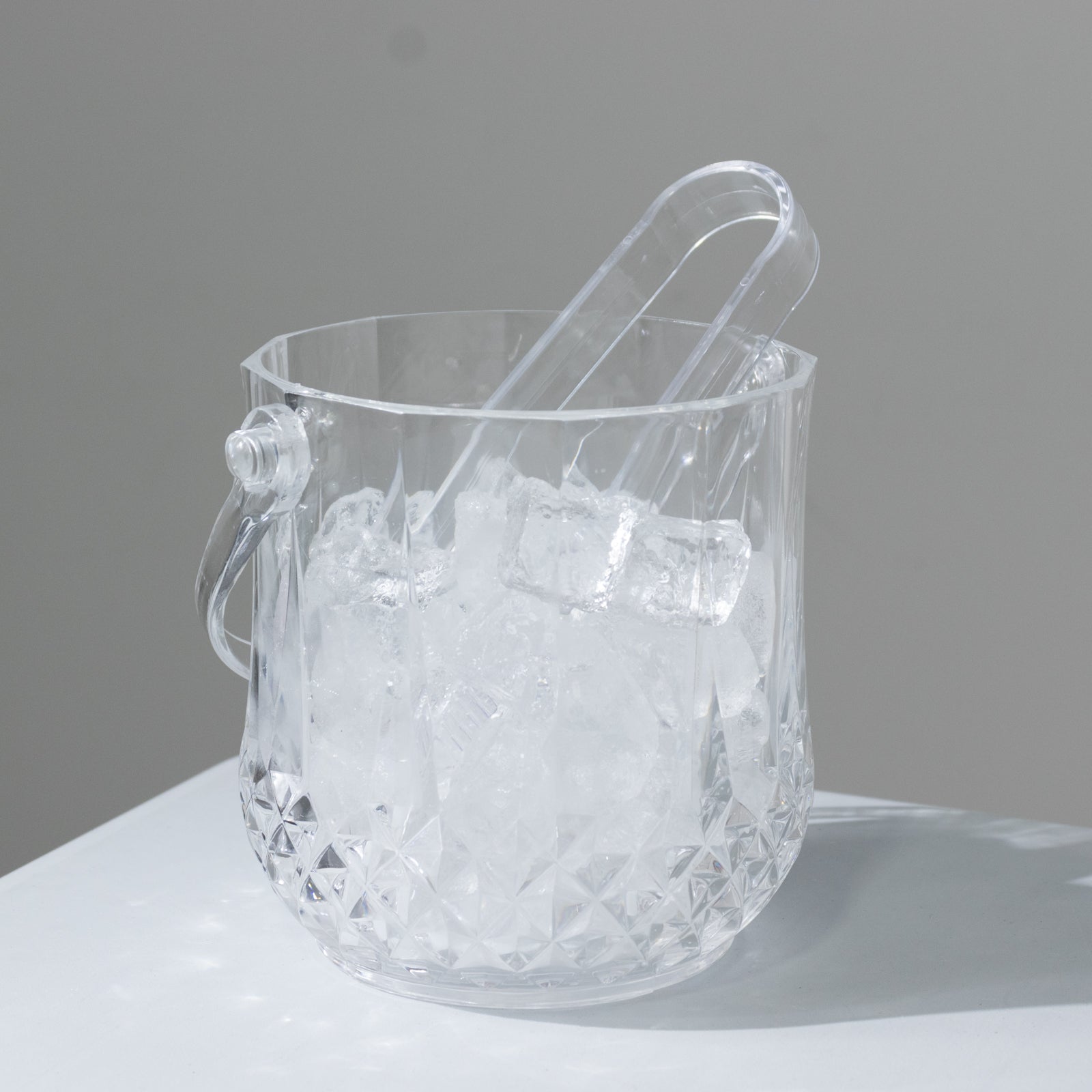 Clear plastic ice bucket with tongs in crystal-cut design, perfect for cocktails.
