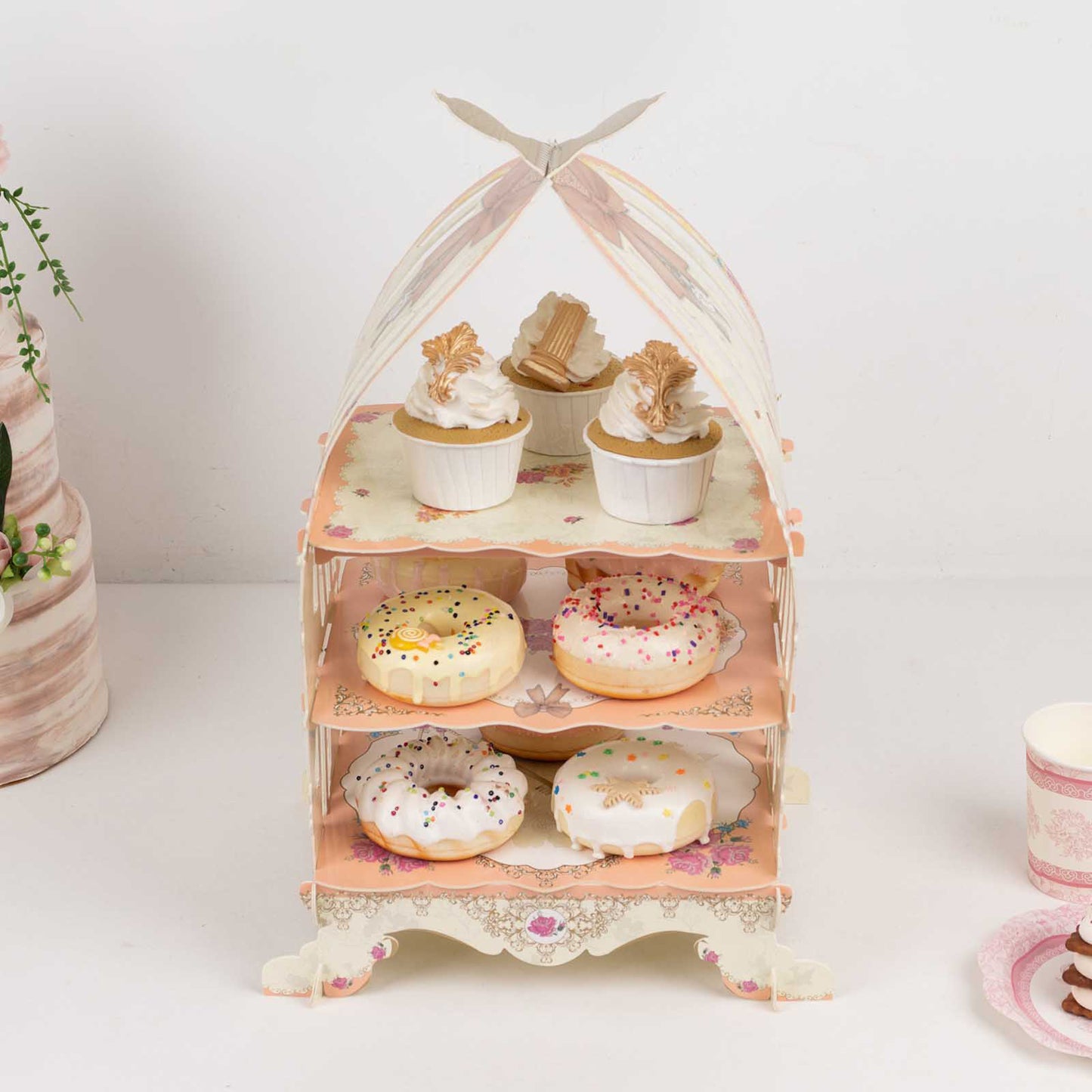 3 Tier white dessert display stand with floral print, decorated with cupcakes and donuts.