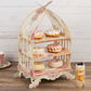 White birdcage dessert display stand with floral print and cake assortment.