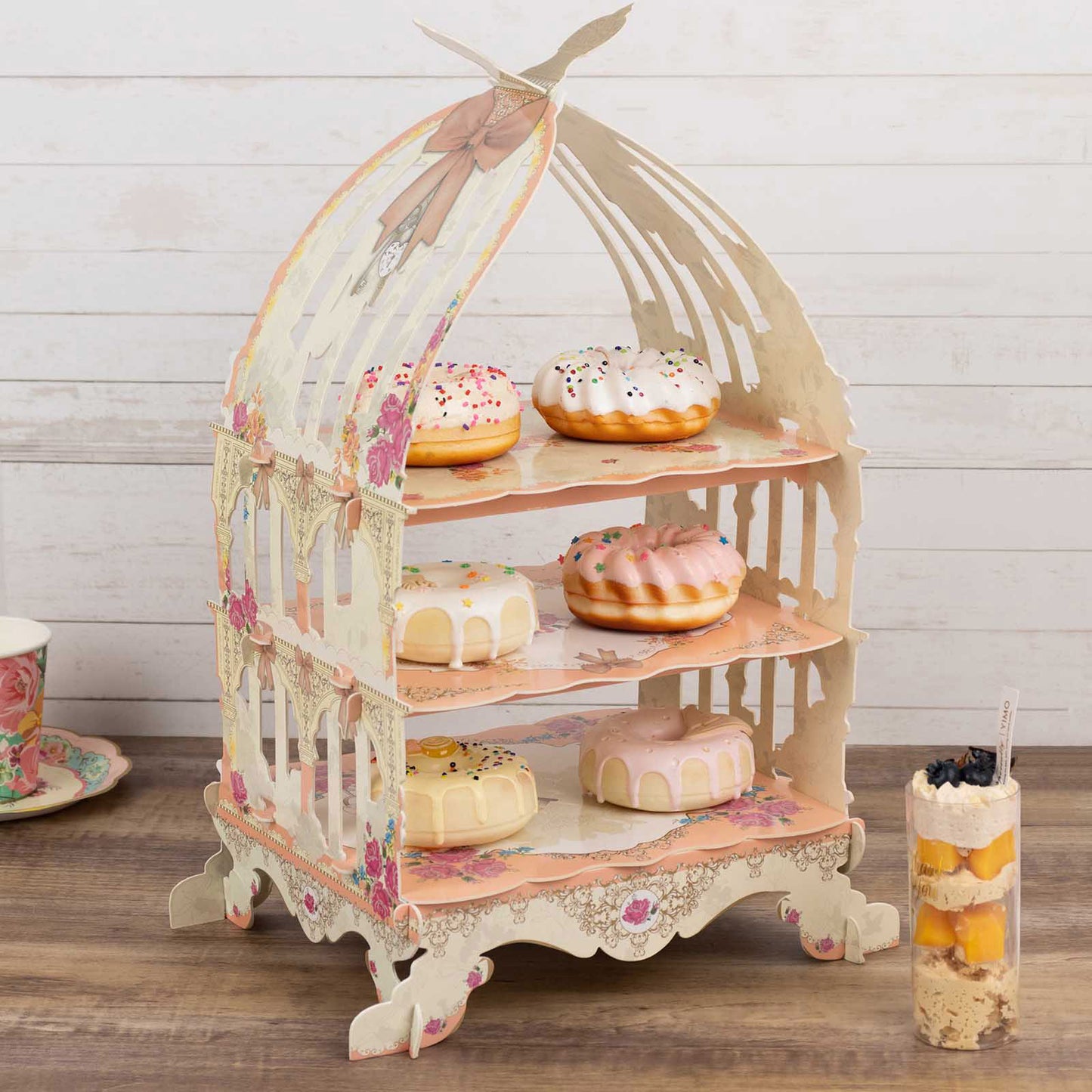 White birdcage dessert display stand with floral print and cake assortment.