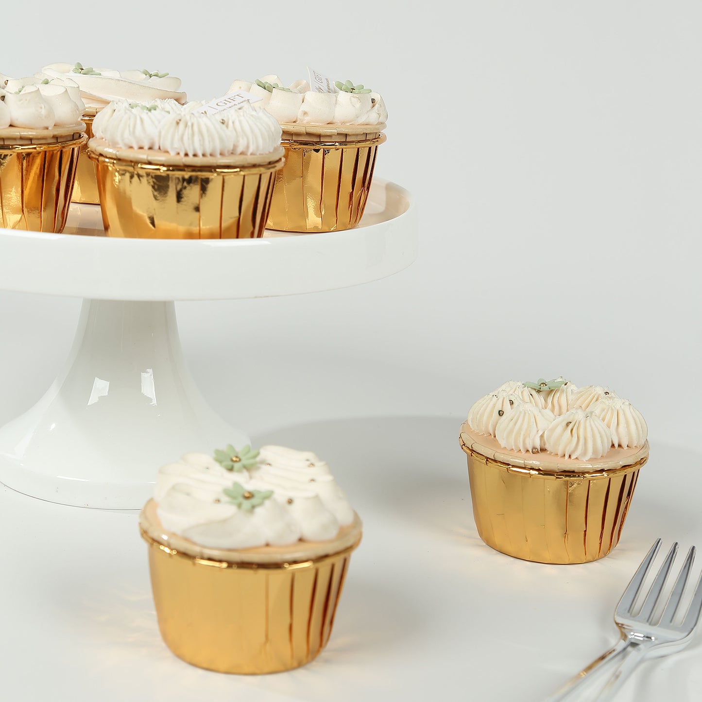 Metallic gold foil cupcake liners with desserts on a white pedestal.