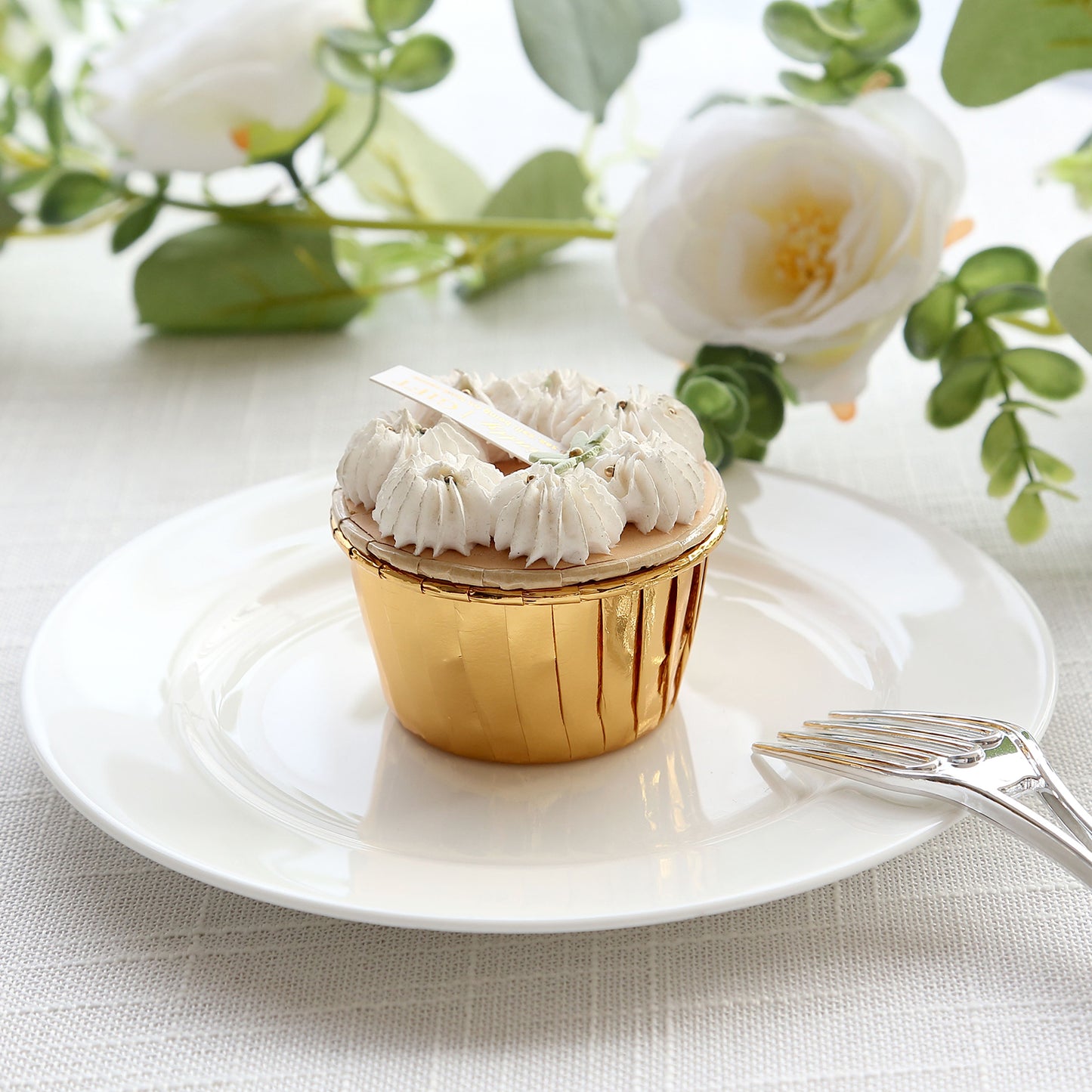 Metallic gold foil baking cup with a white frosted dessert on a plate.