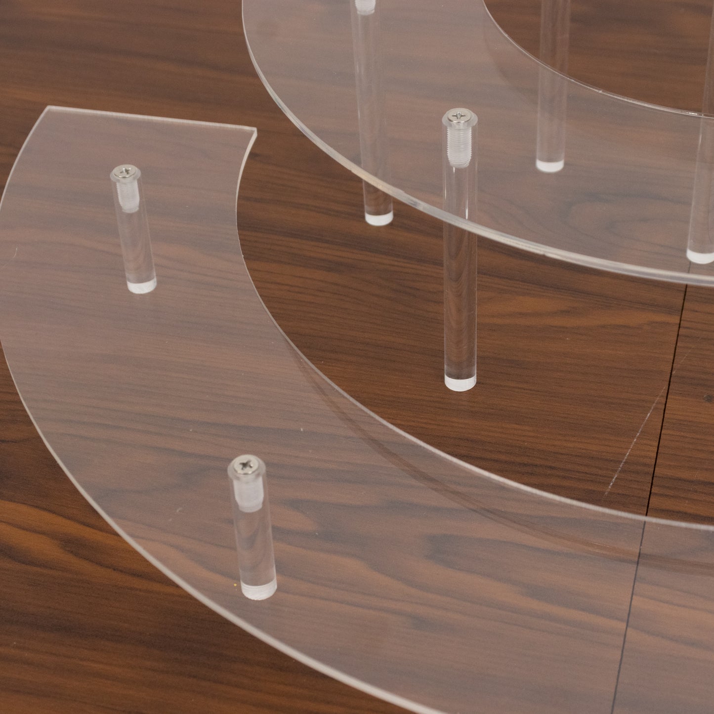 Clear acrylic half-moon display riser stands on a wooden surface.