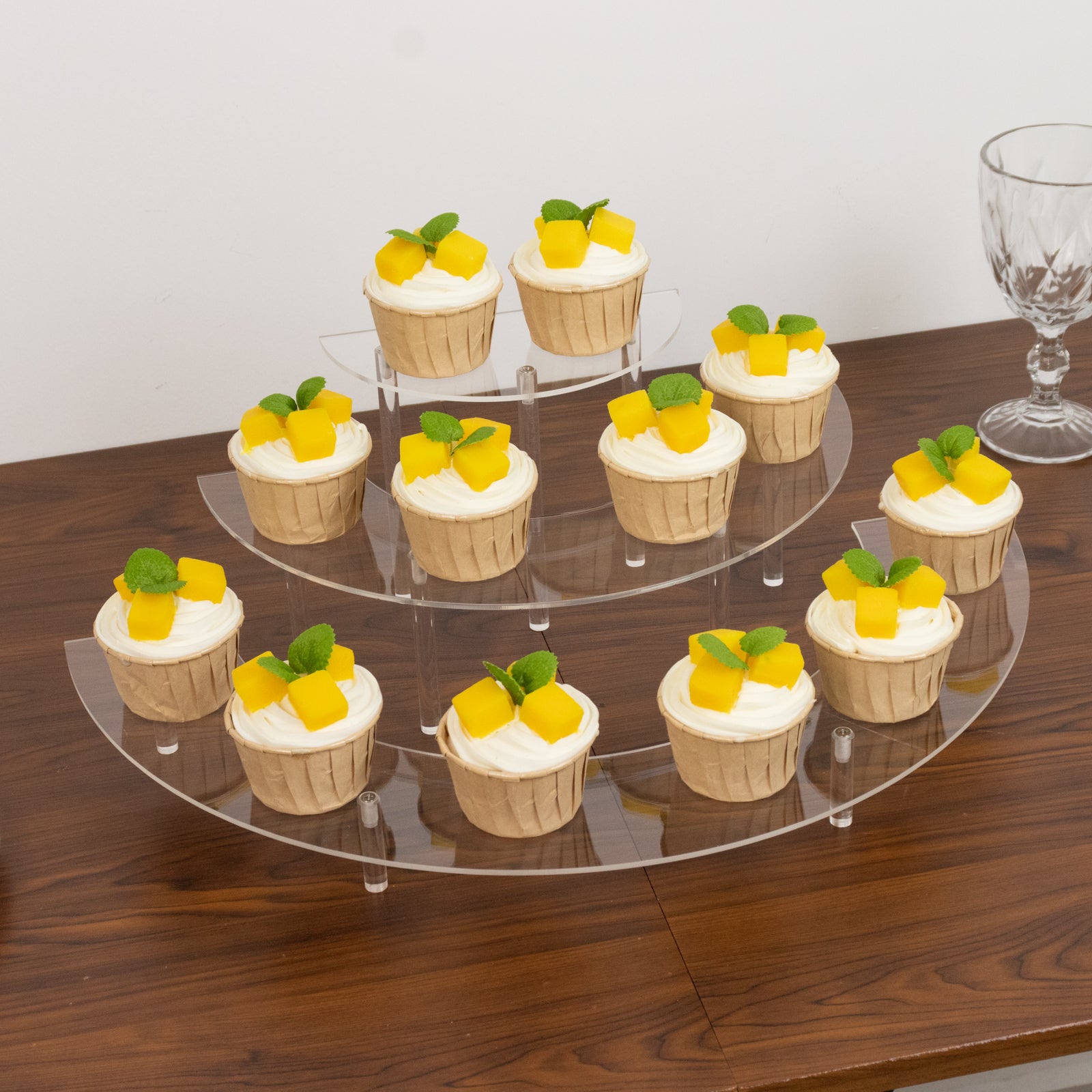Clear acrylic half-moon display risers with desserts on a wooden table.