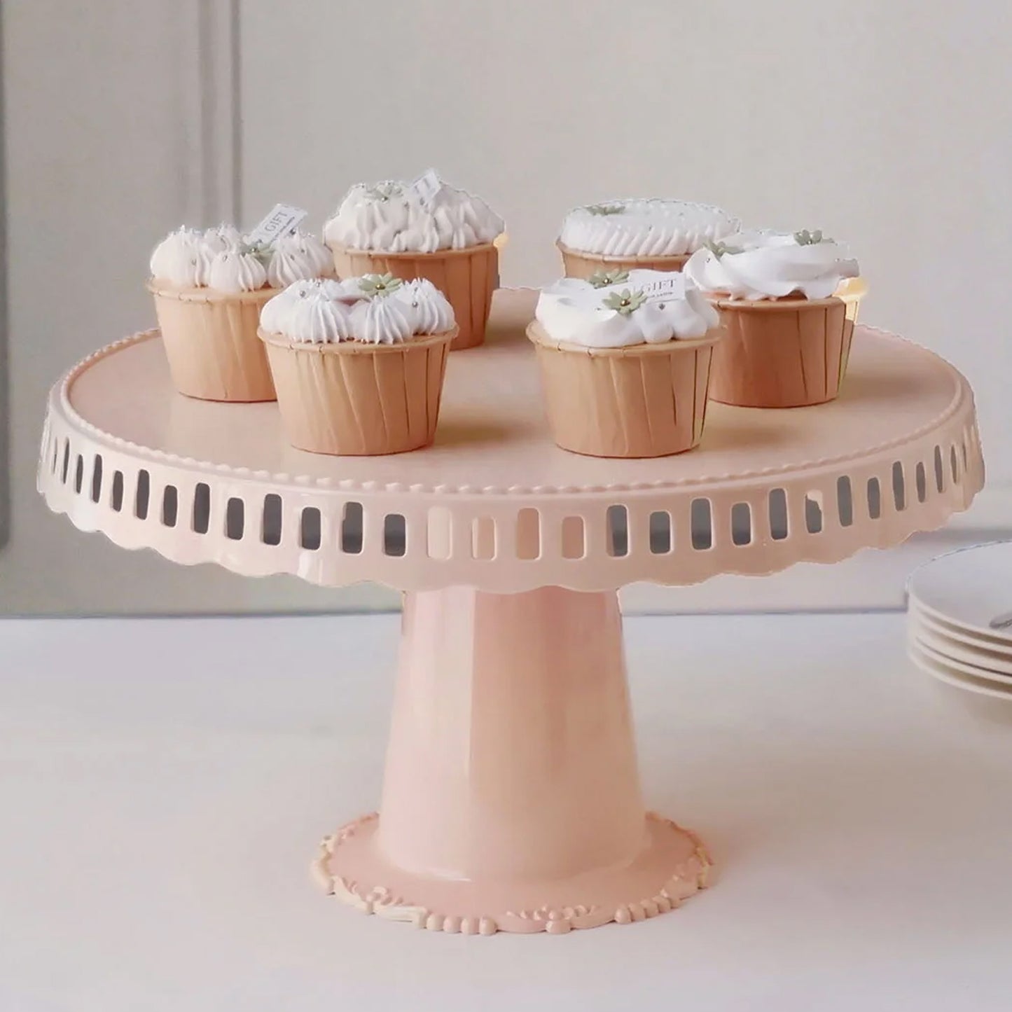 Blush round footed cake stand with cupcakes on a white background.