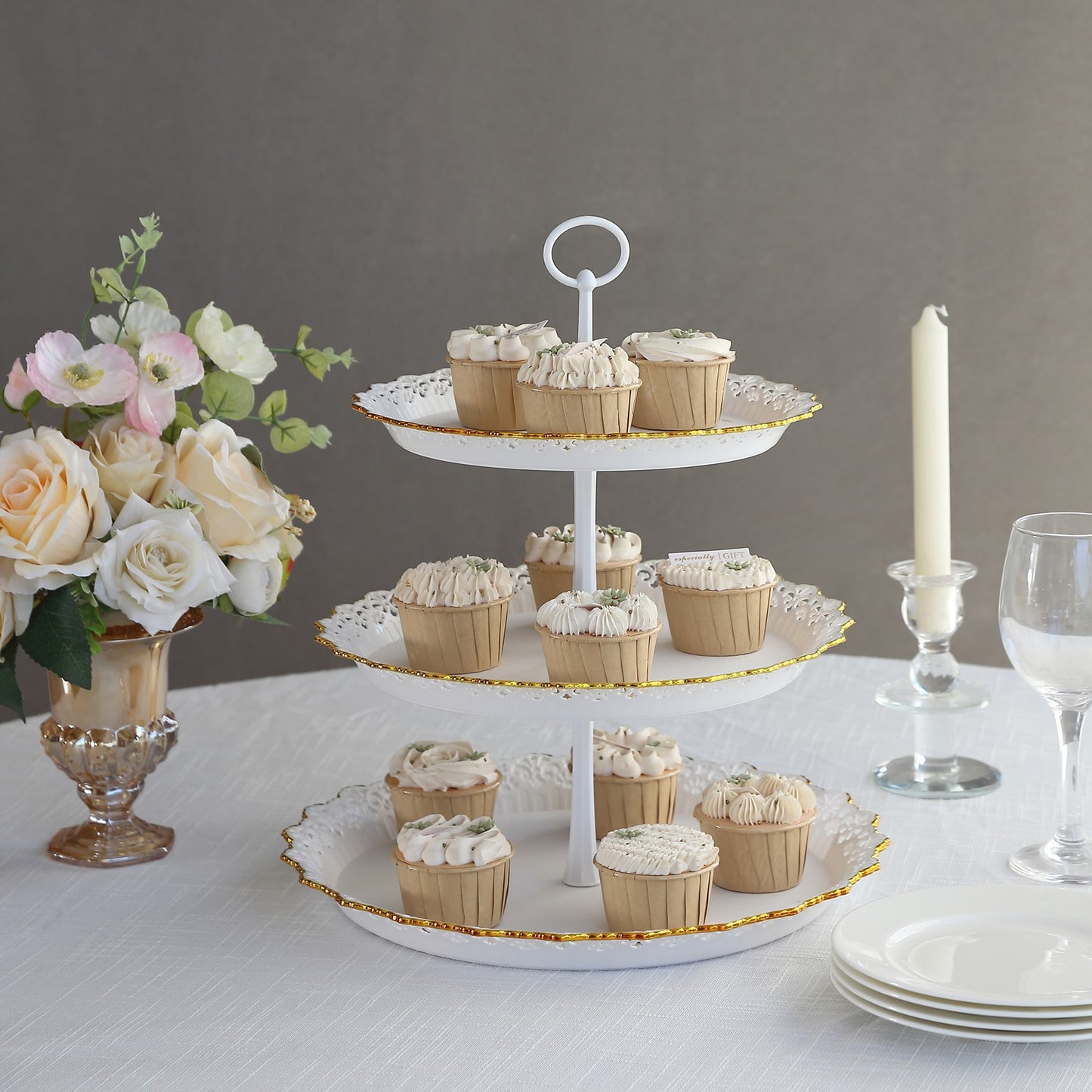 15" white 3-tier cupcake stand with gold rim displaying cupcakes on a table.