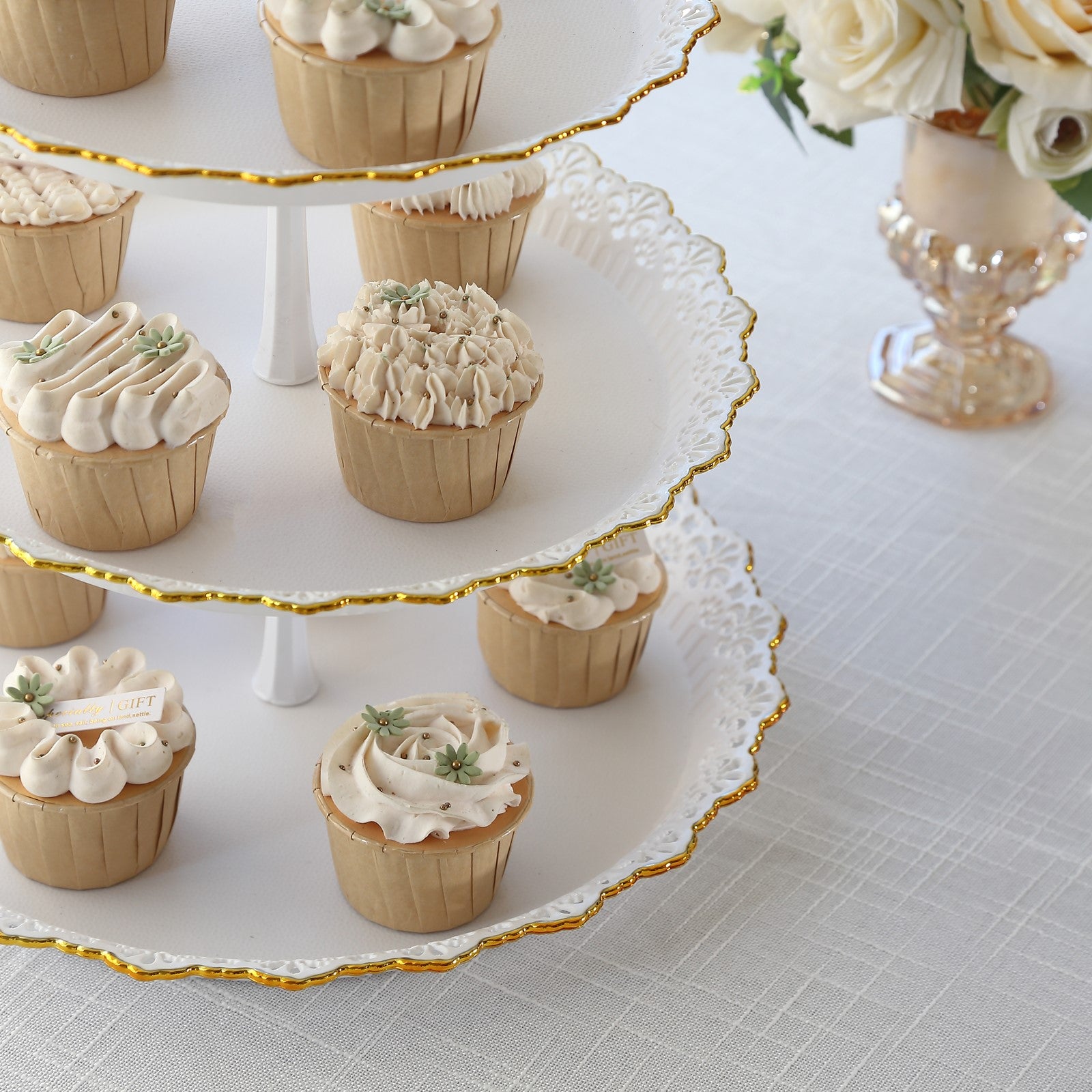 White 3-tier cupcake stand with gold rim, holding beige frosted cupcakes.