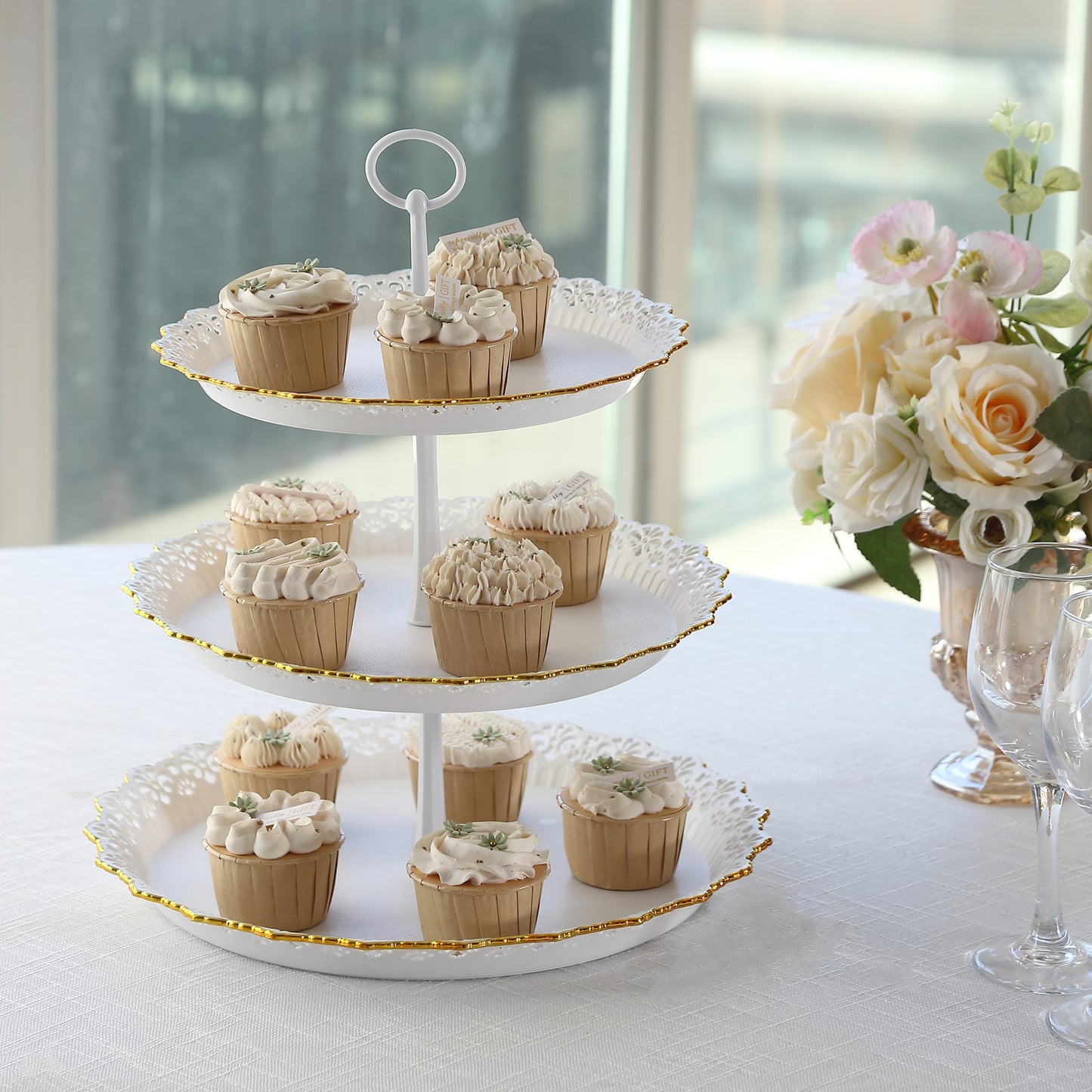 White 3-tier cupcake stand with lace cut gold rim, holding decorated desserts.