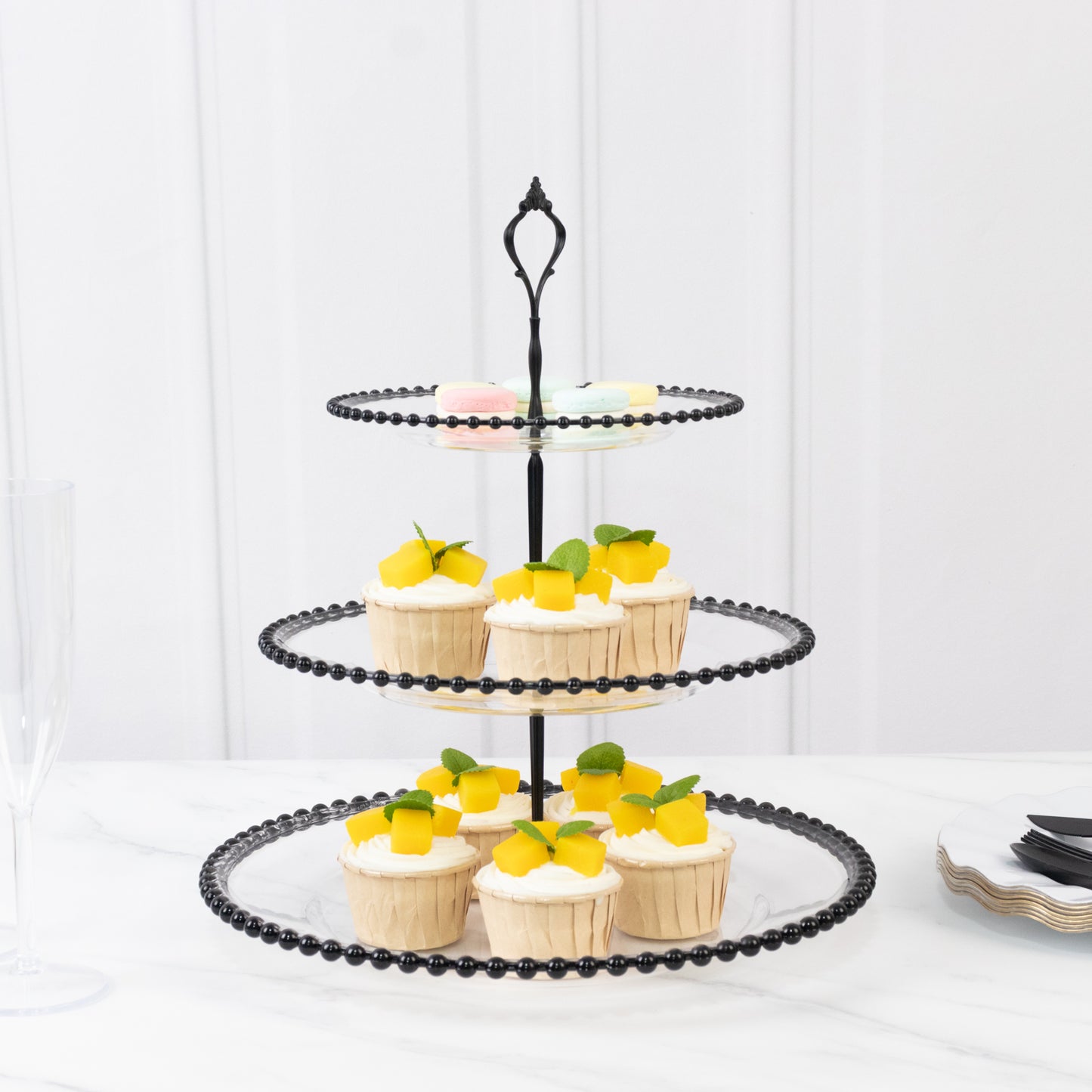 Clear 3-tier dessert display stand with black beaded rim and cupcakes.