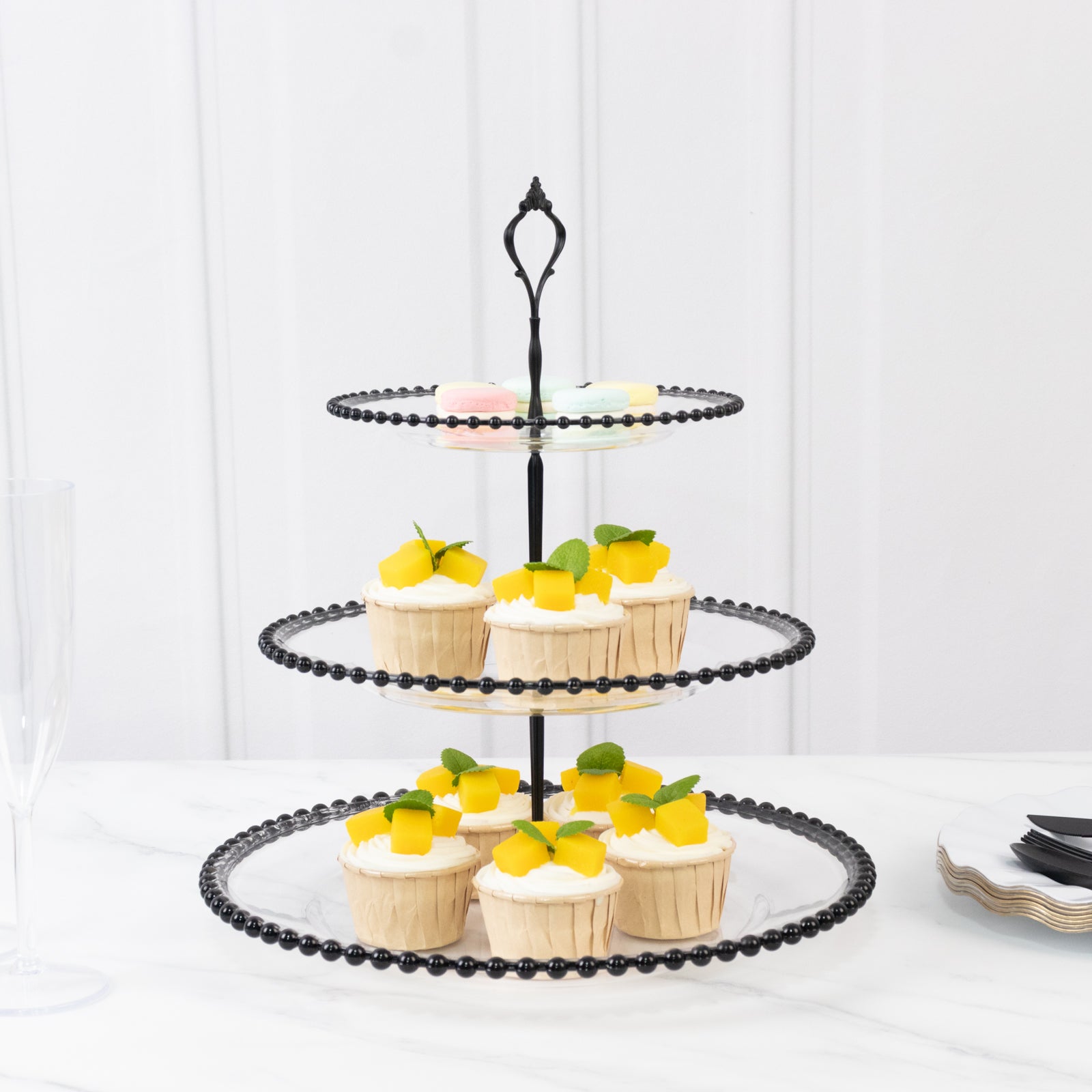 Clear 3-tier dessert display stand with black beaded rim and cupcakes.