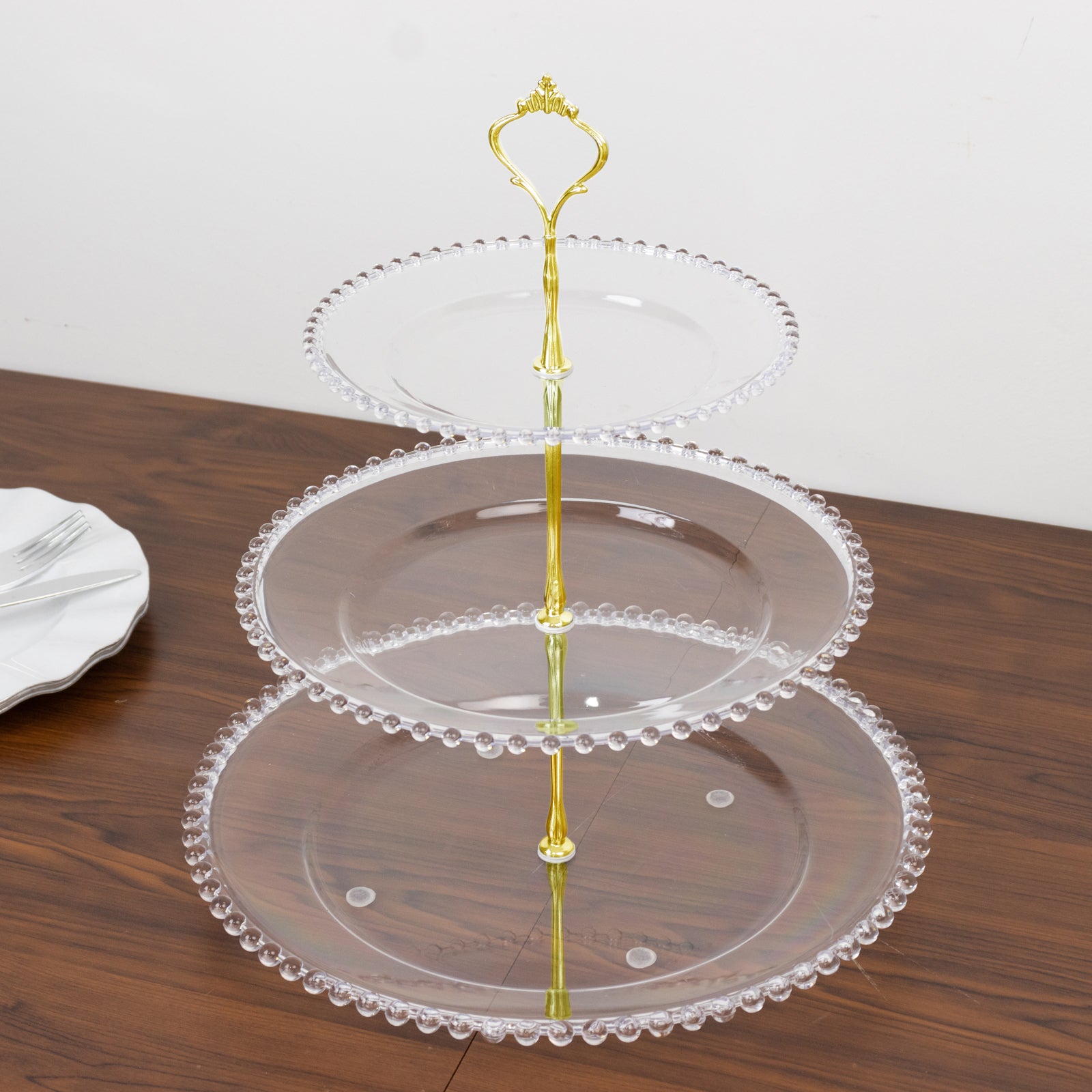 Clear 3-tier plastic dessert display stand with beaded rim and top handle.