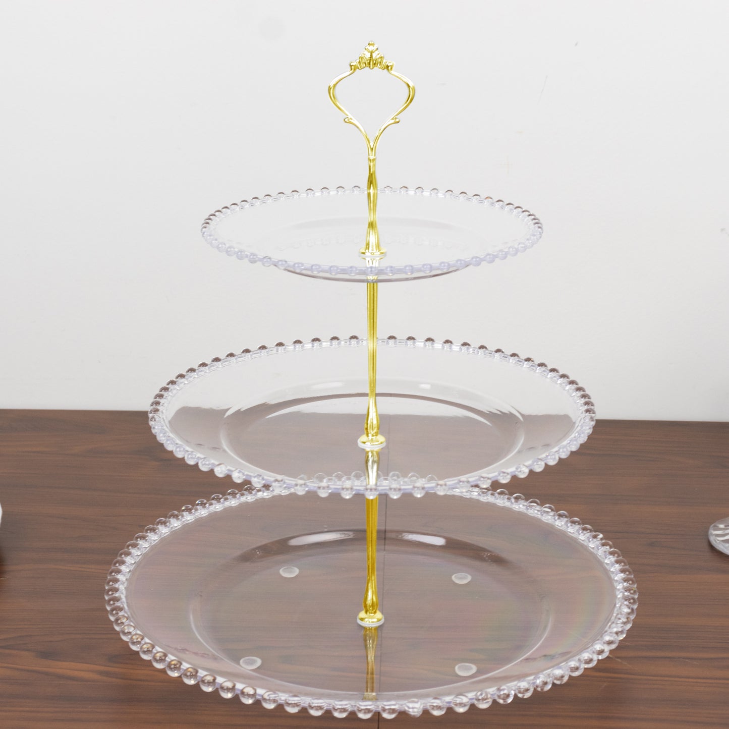 Clear 3-tier dessert display stand with beaded rim and gold handle.