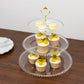 Clear 3-tier dessert display stand with cupcakes and macarons on a wooden table.