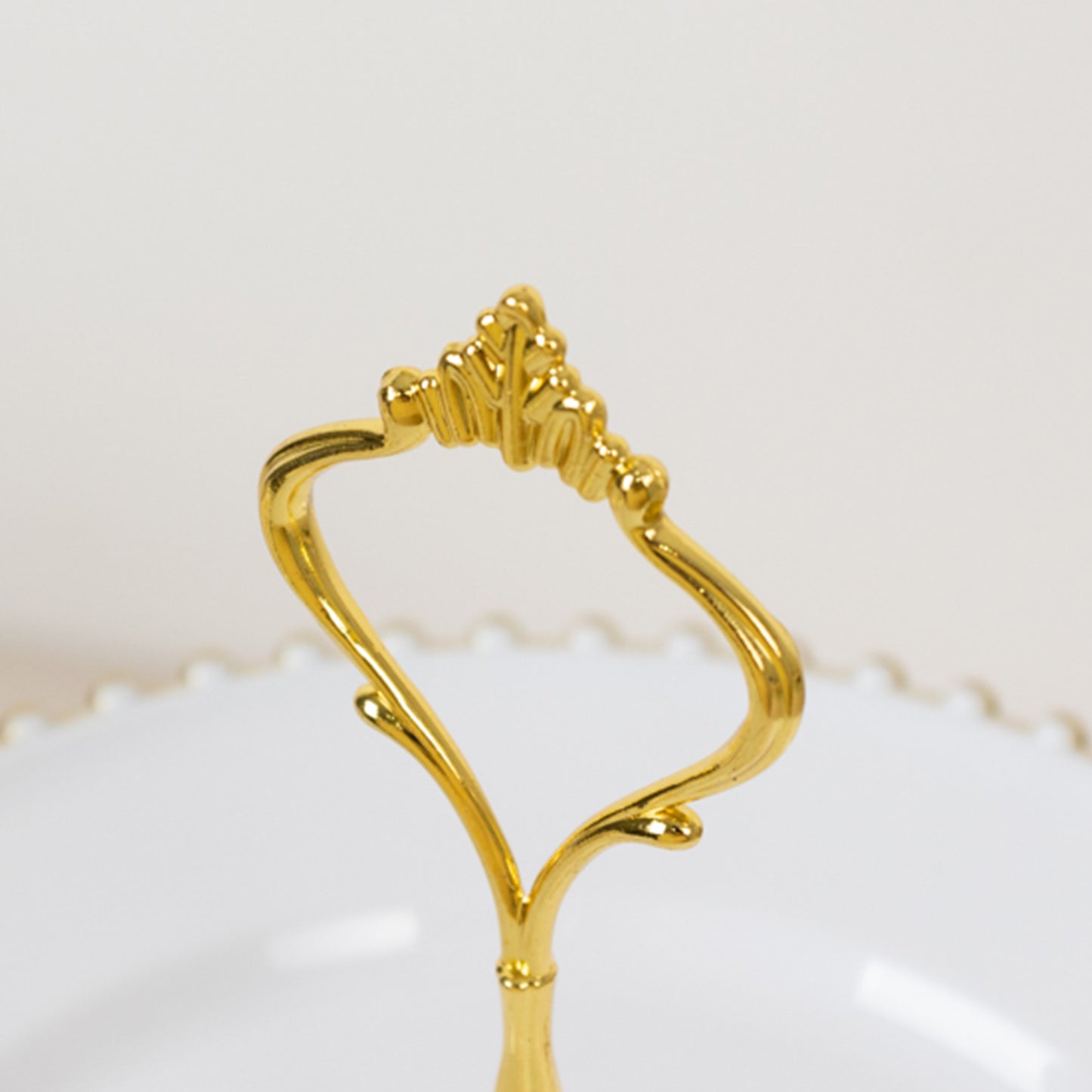 Gold handle of a white 3-tier dessert display stand with beaded rim.