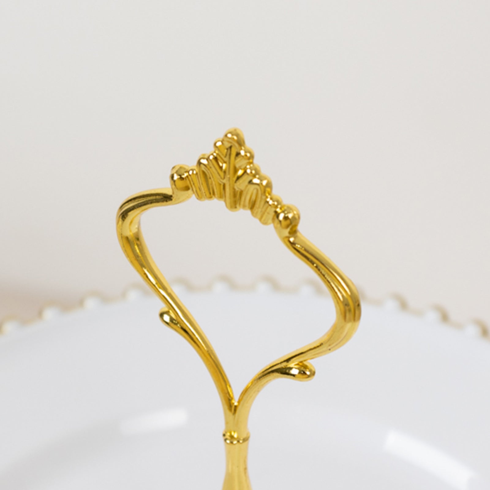 Gold handle of a white 3-tier dessert display stand with beaded rim.