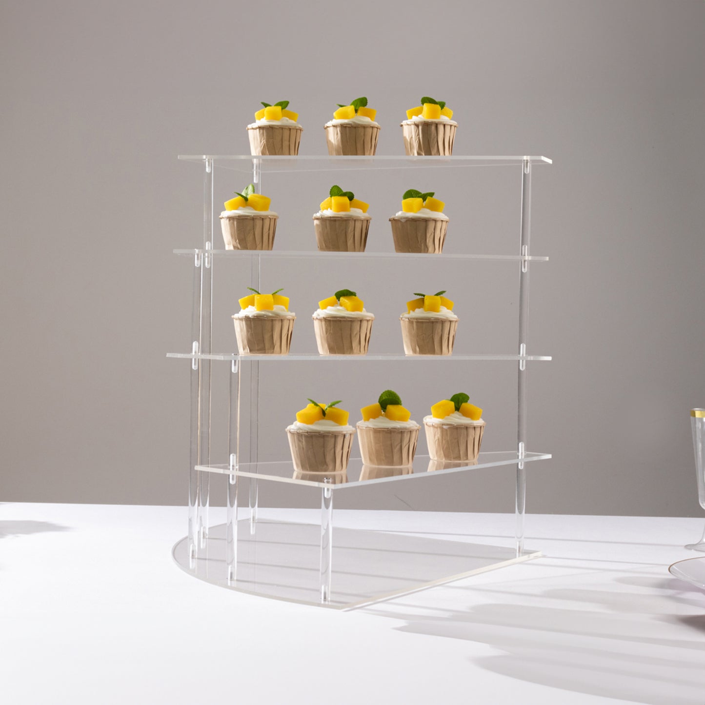 Clear acrylic 4-tier cupcake stand displaying desserts on a white background.