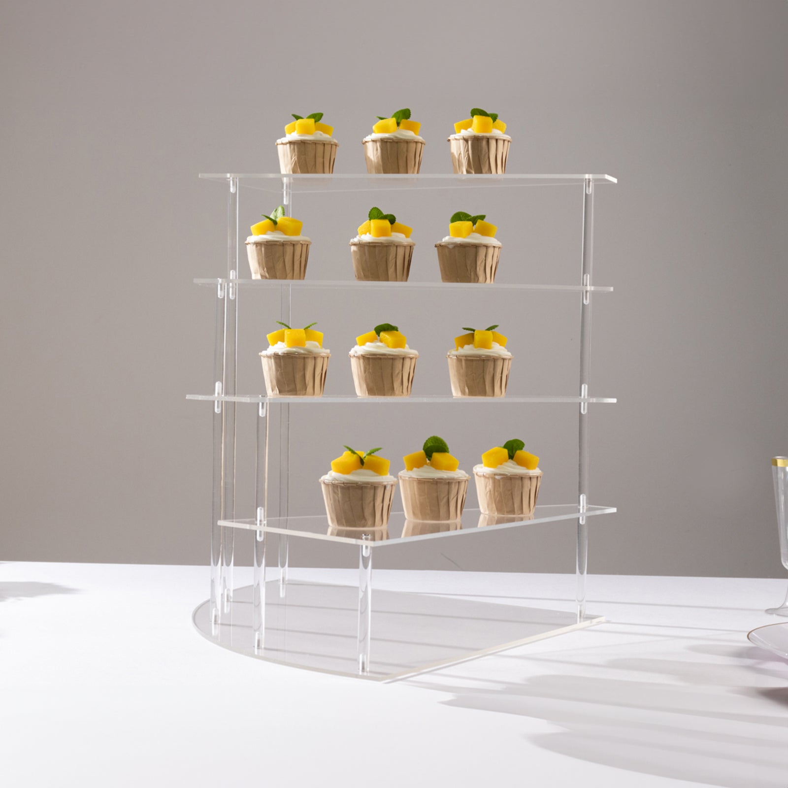 Clear acrylic 4-tier cupcake stand displaying desserts on a white background.