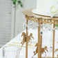 Gold carousel cake stand with hanging acrylic beads for dessert display.