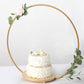 Gold floral hoop cake stand with wooden base displaying a decorated cake.