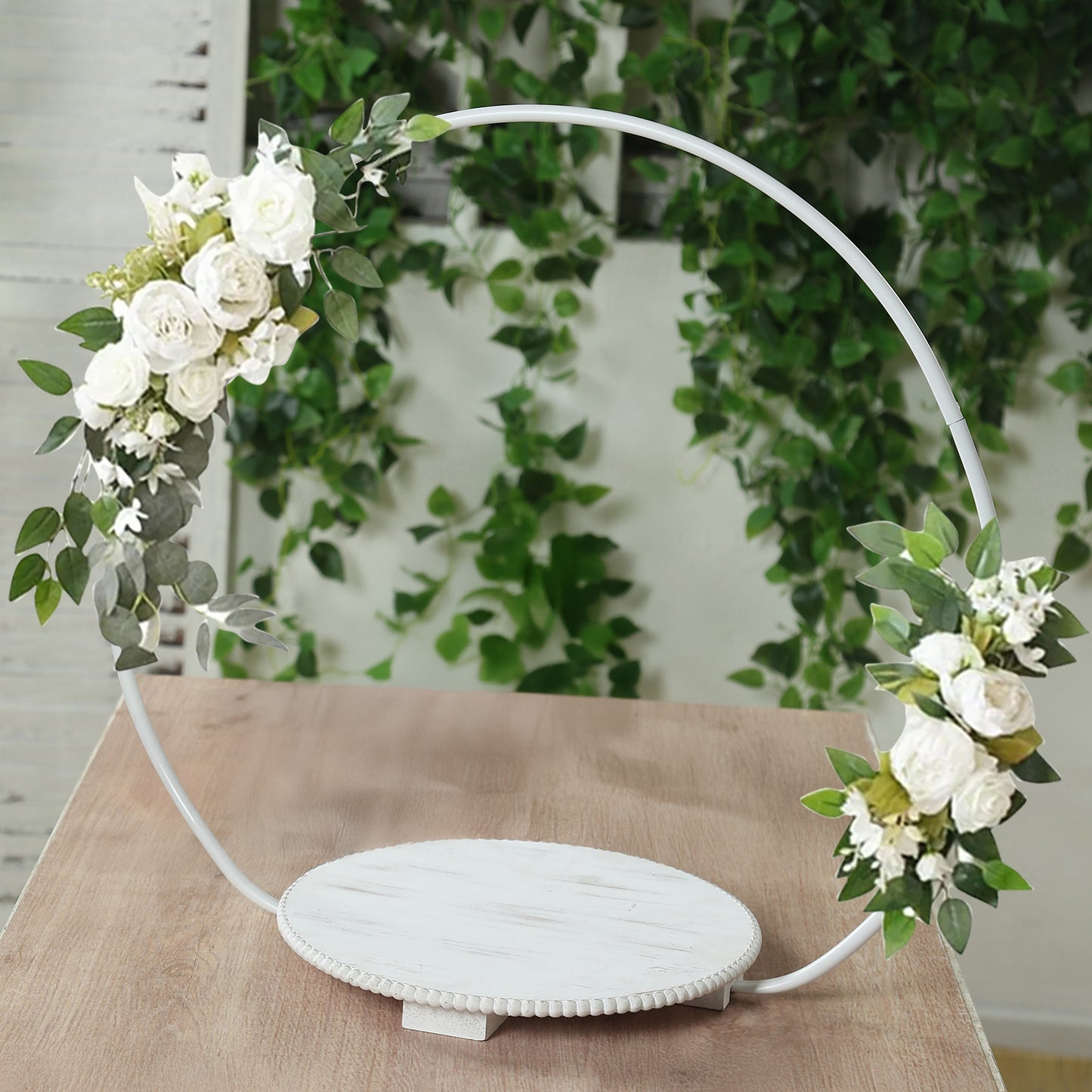 White floral hoop cake stand with beaded wooden base and greenery.