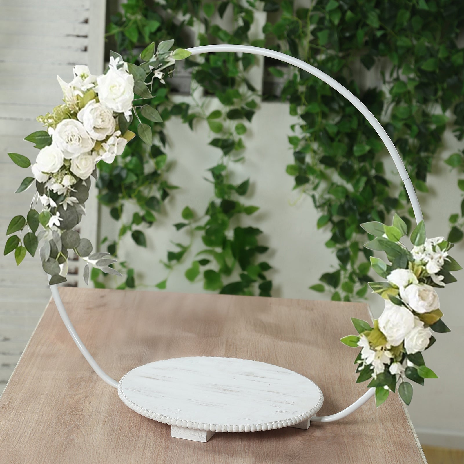 White floral hoop cake stand with beaded wooden base and greenery.