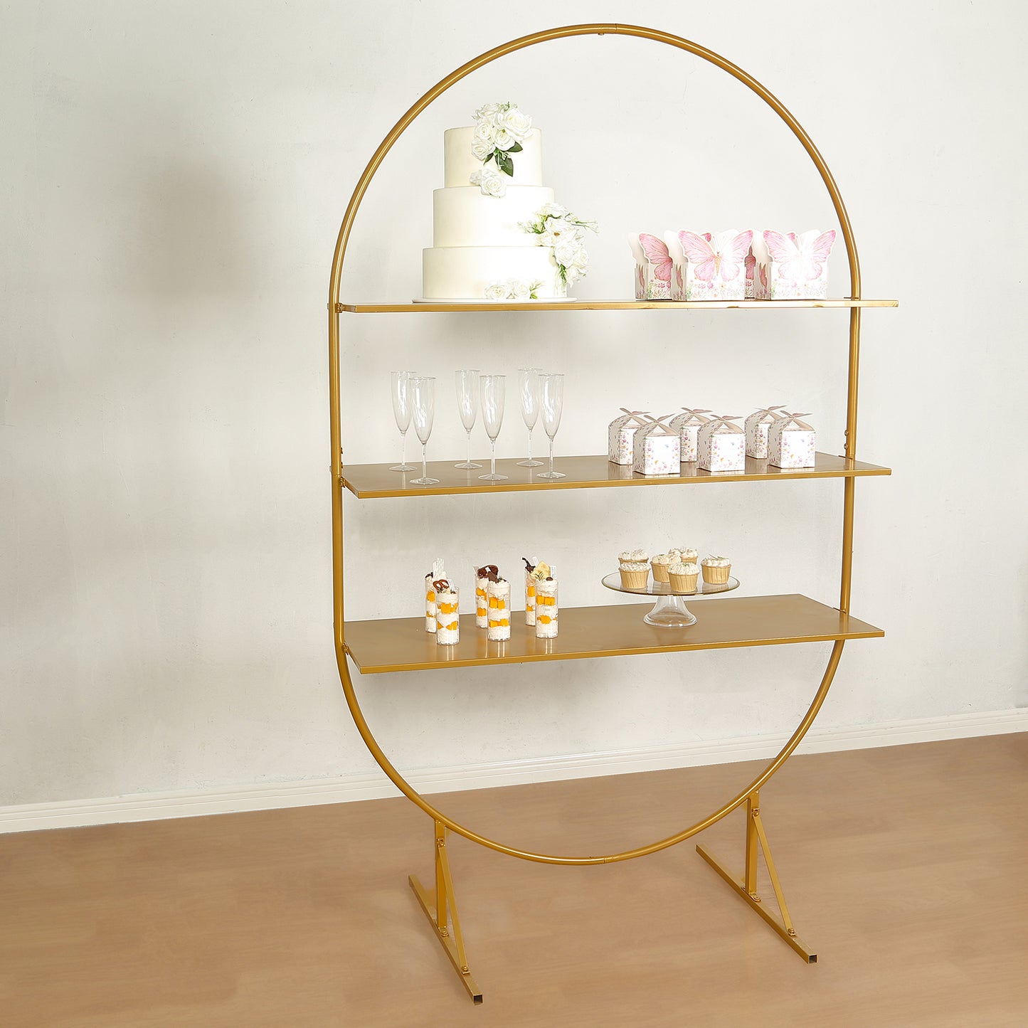 Gold metal arch cake display stand with three tiers for desserts and cupcakes.