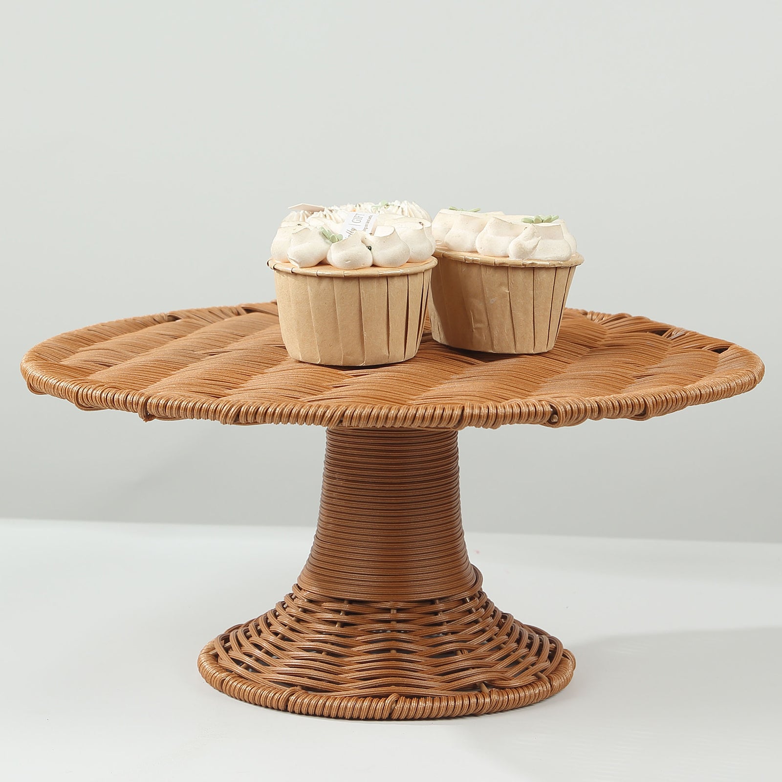 Natural wicker pedestal cupcake stand with two frosted cupcakes on top.