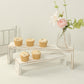 Whitewash wooden display risers with cupcakes and flowers on a table.