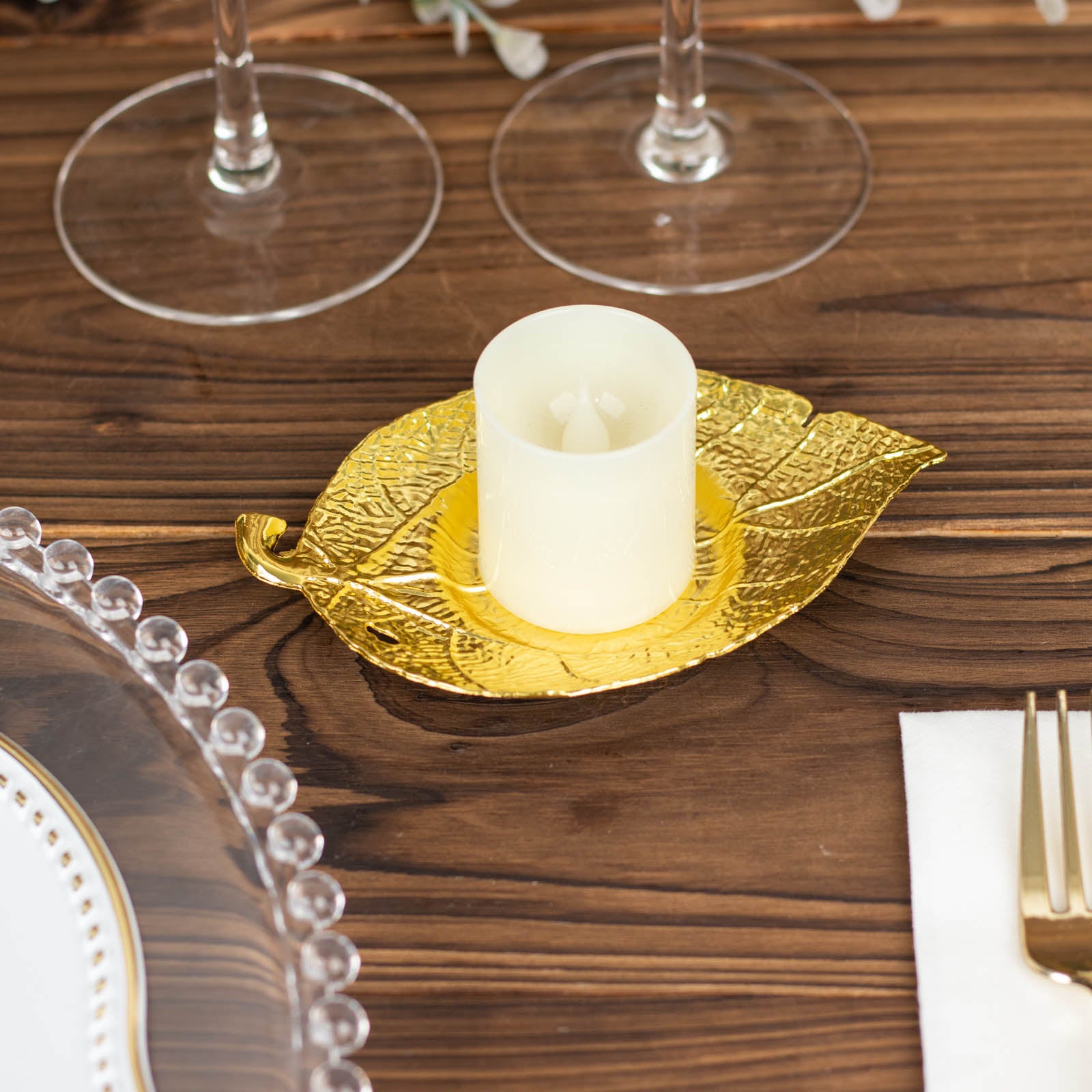 Shiny gold metal maple leaf tealight candle holder on a wooden table.