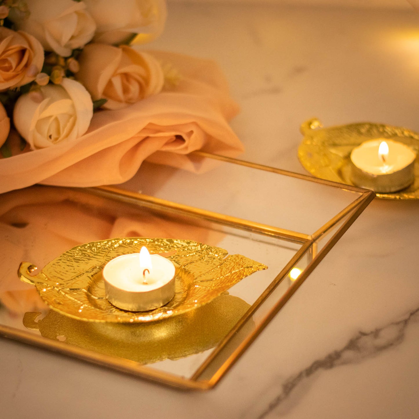 Shiny gold metal maple leaf tealight candle holders on a reflective surface.