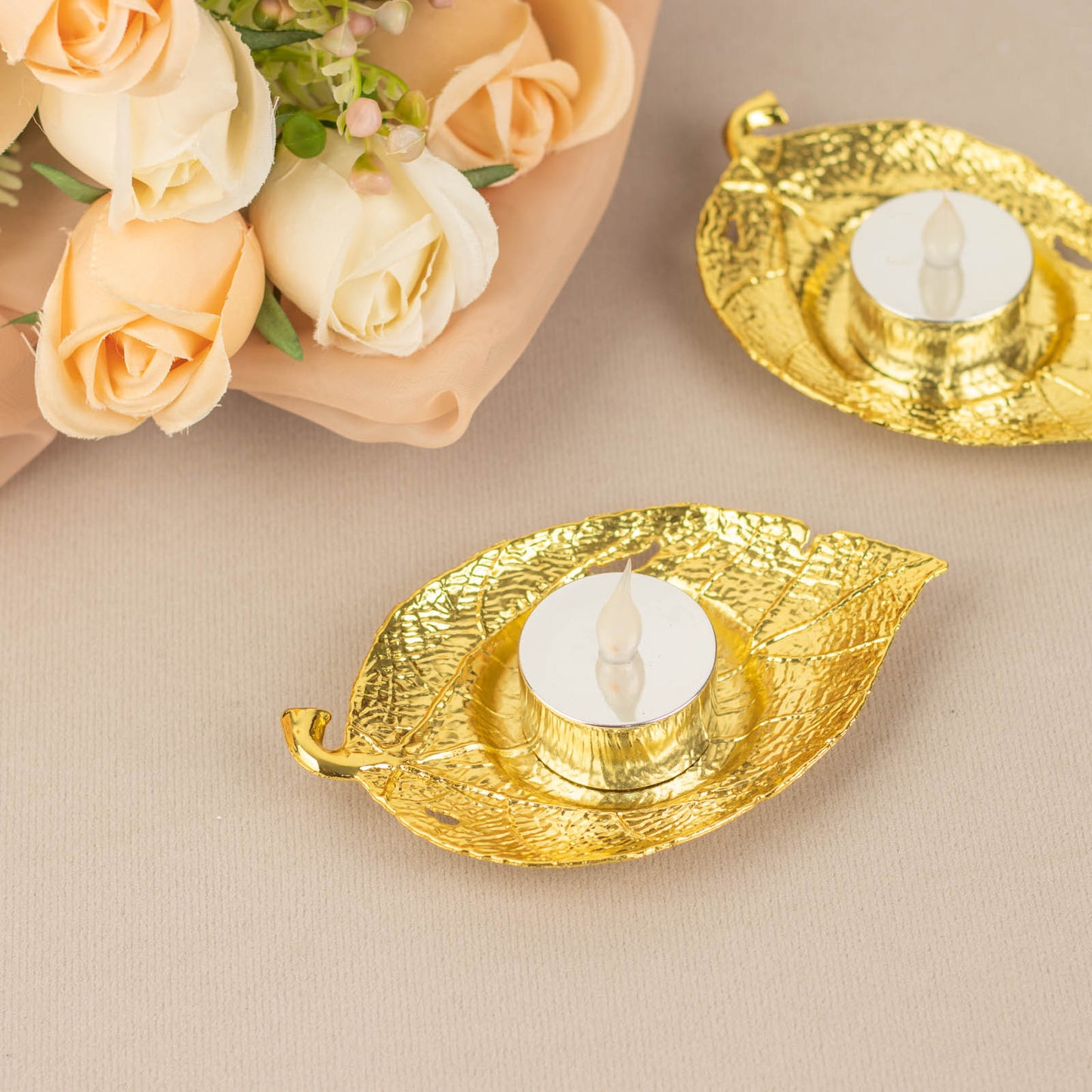Shiny gold metal maple leaf tealight candle holders on a neutral background.