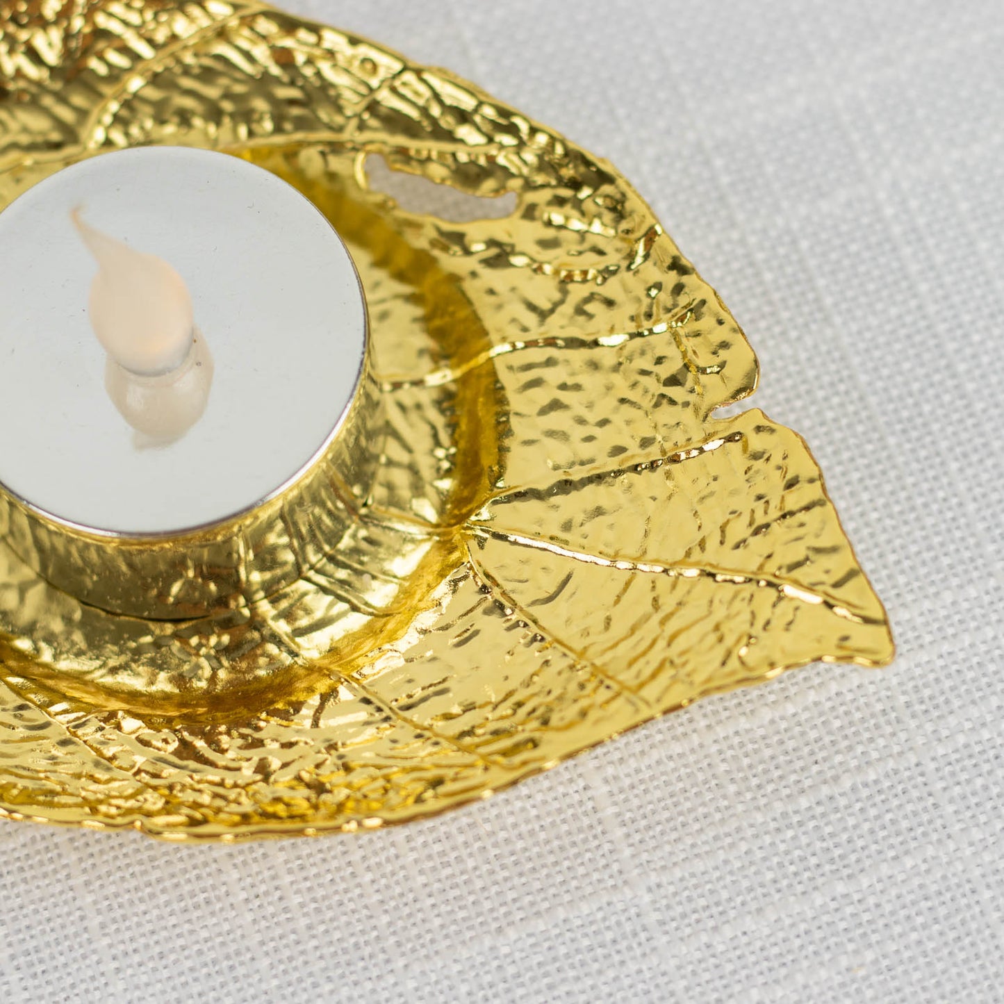 Shiny gold metal maple leaf tealight candle holder on a white background.