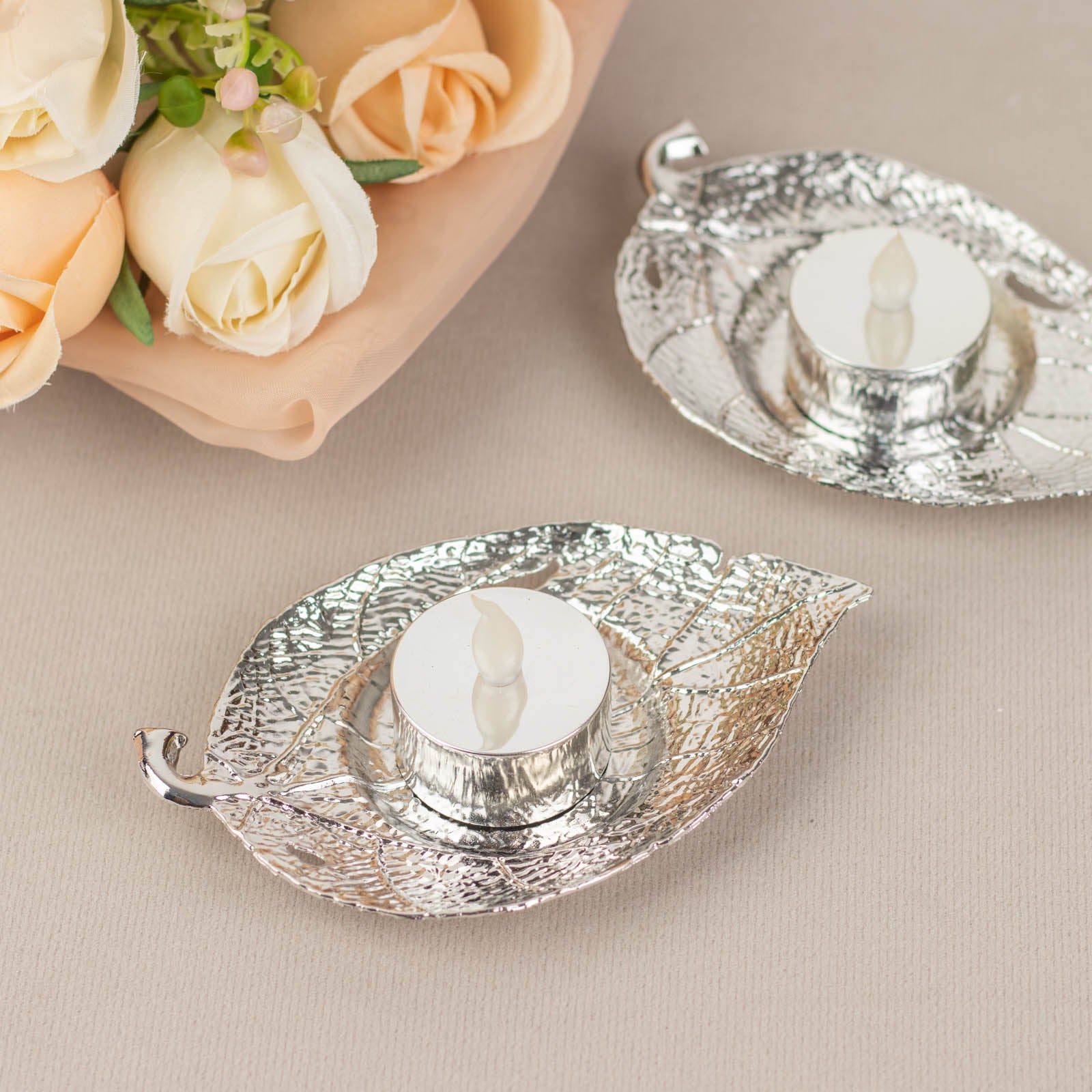 Shiny silver metal maple leaf tealight candle holders on a neutral background.