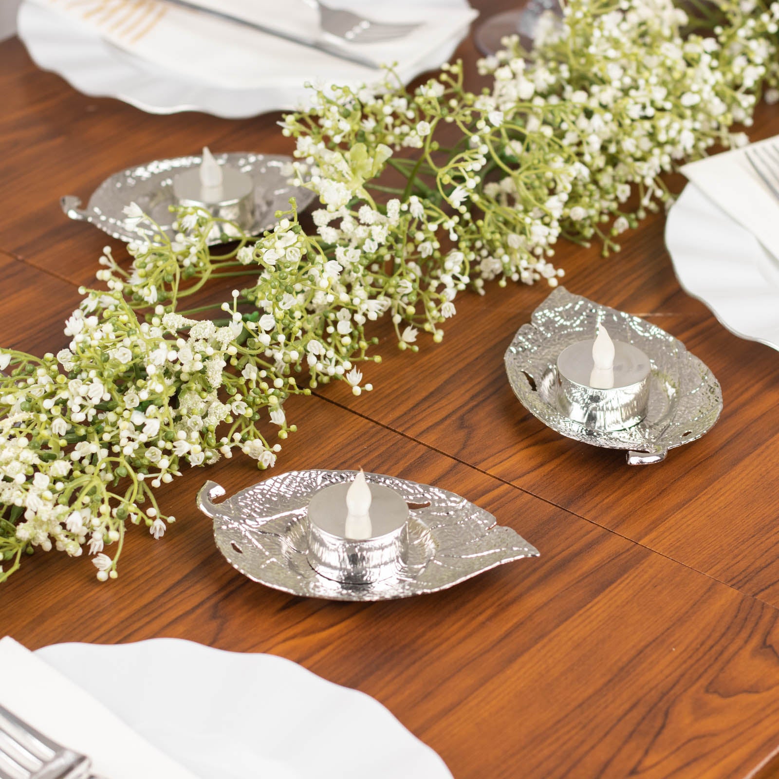 Shiny silver metal maple leaf tealight candle holders on a table setting.