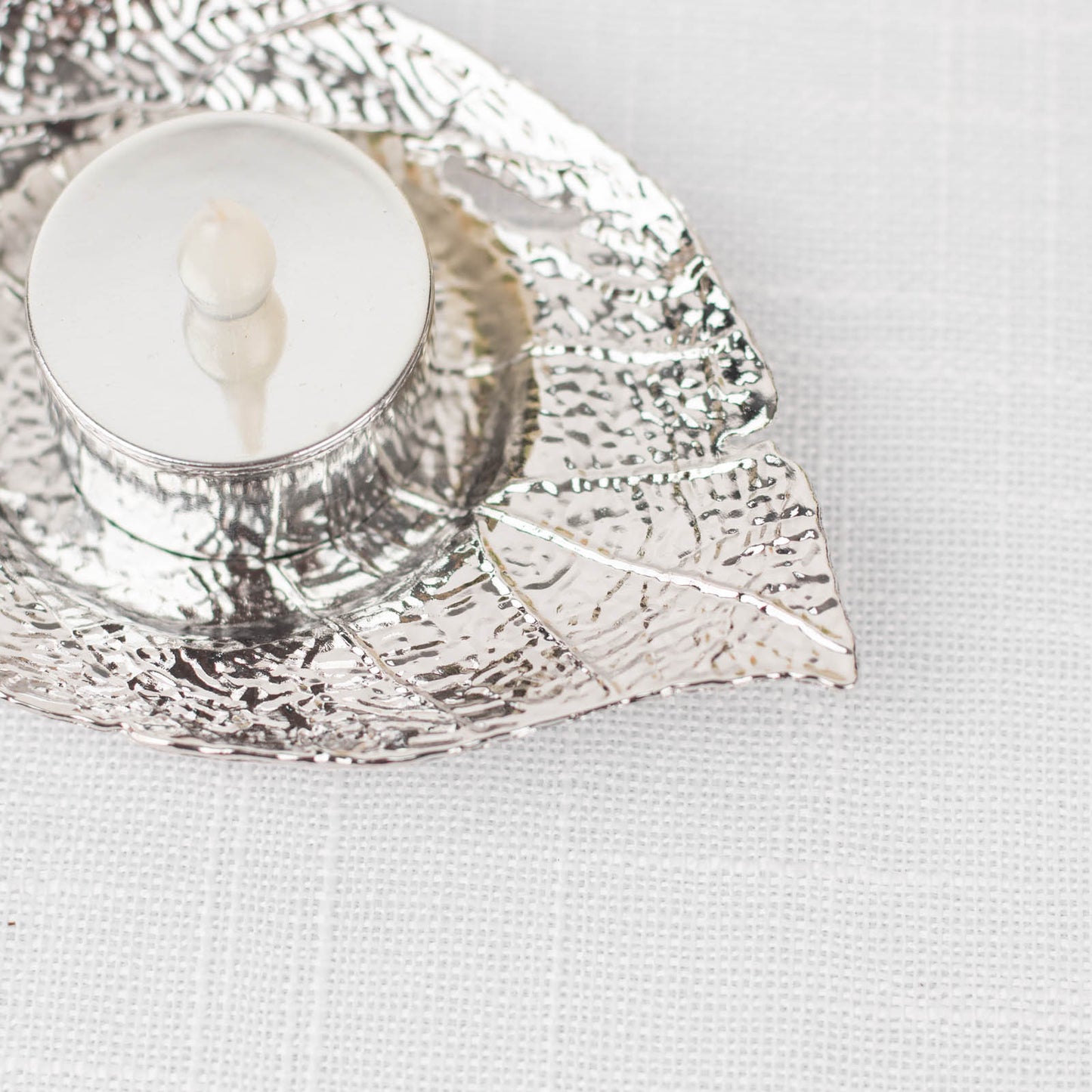 Shiny silver metal maple leaf tealight candle holder on a white background.